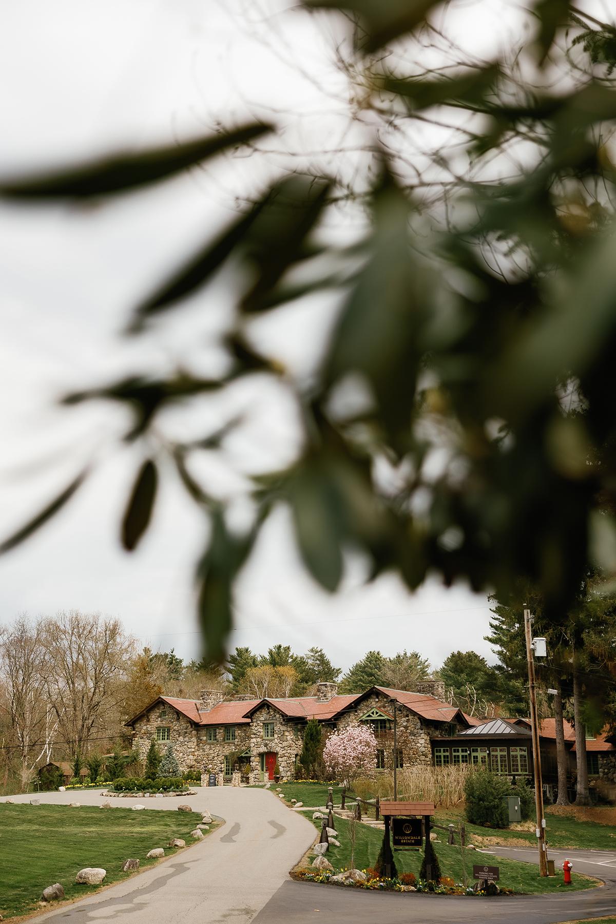 Rustic lodge with red roof, surrounded by trees, under cloudy sky.
