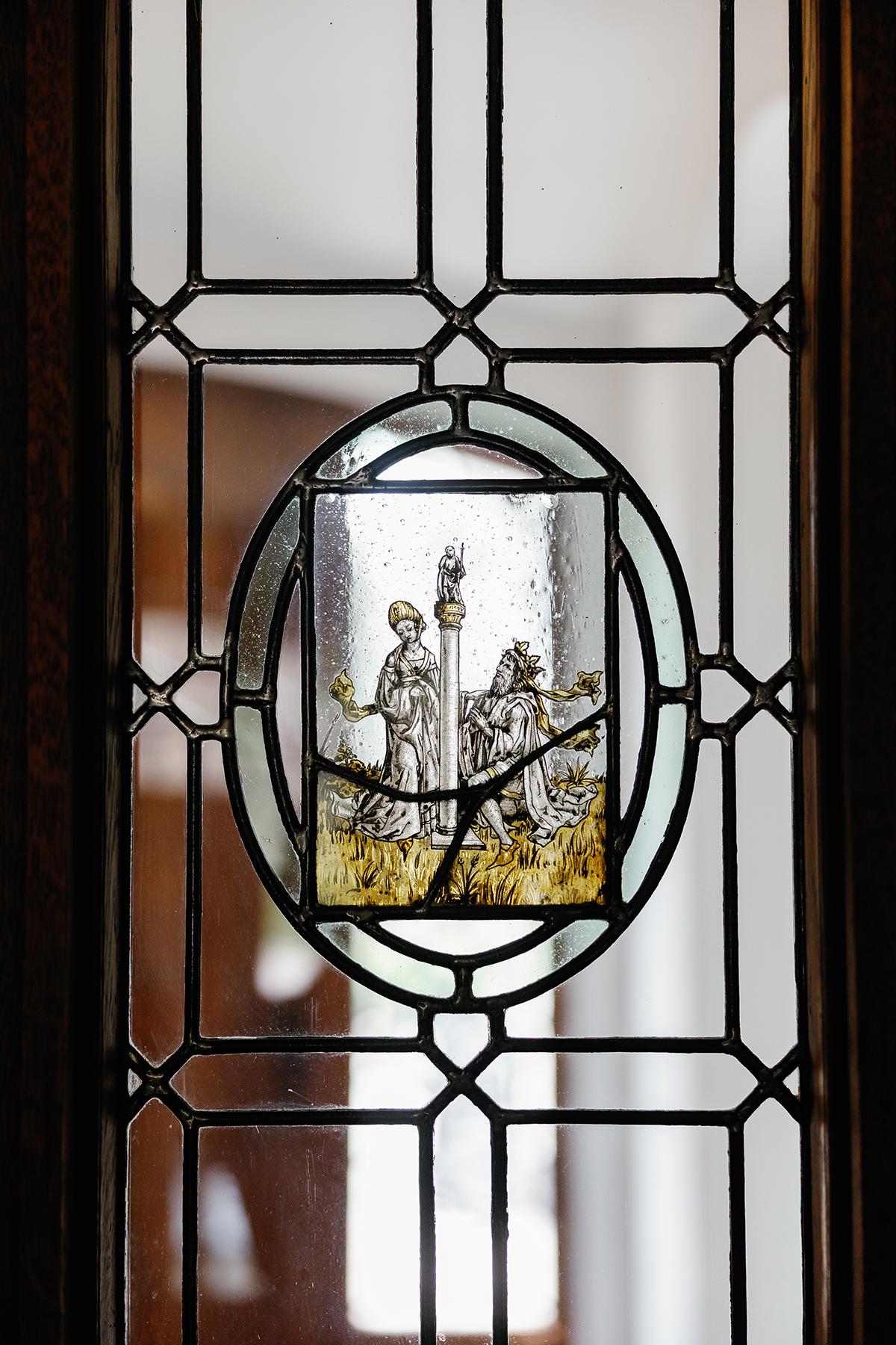 Stained glass panel depicting figures, framed by geometric patterns.