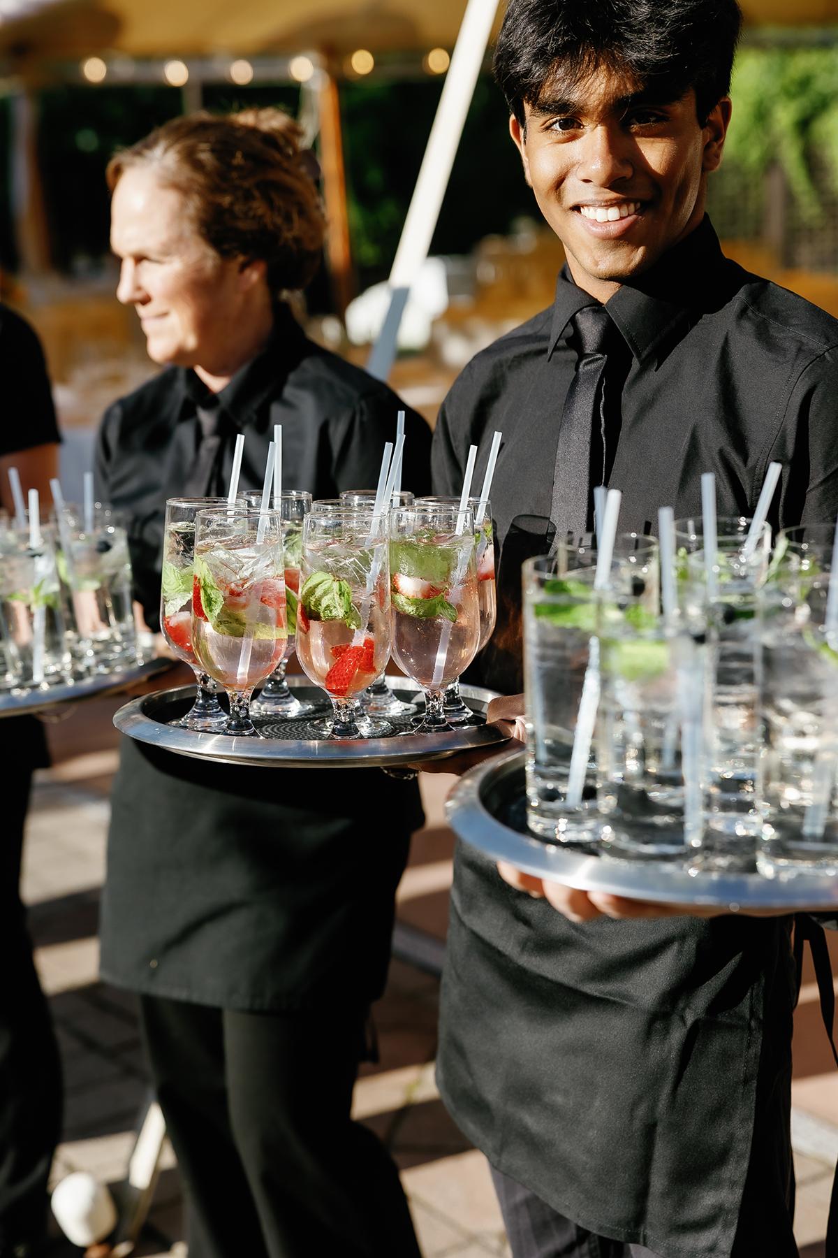 Waitstaff carrying trays of cocktails with mint and lime.