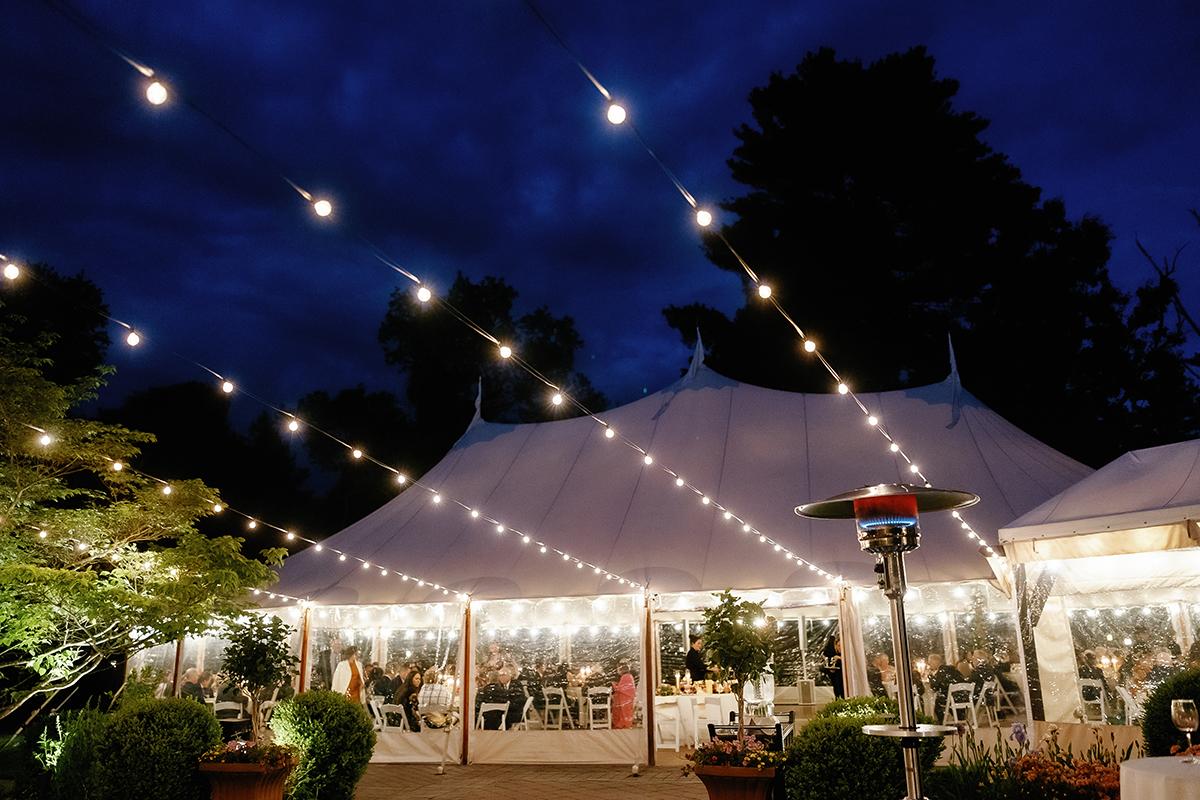 White tent with string lights glowing at night, surrounded by trees.