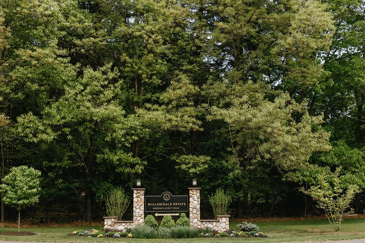 Stone sign in front of lush green trees and plants.