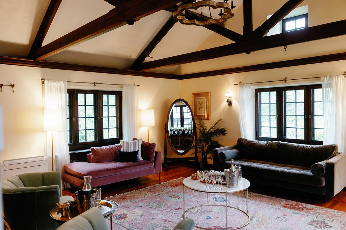 Cozy living room with dark beams, sofas, and a round mirror.