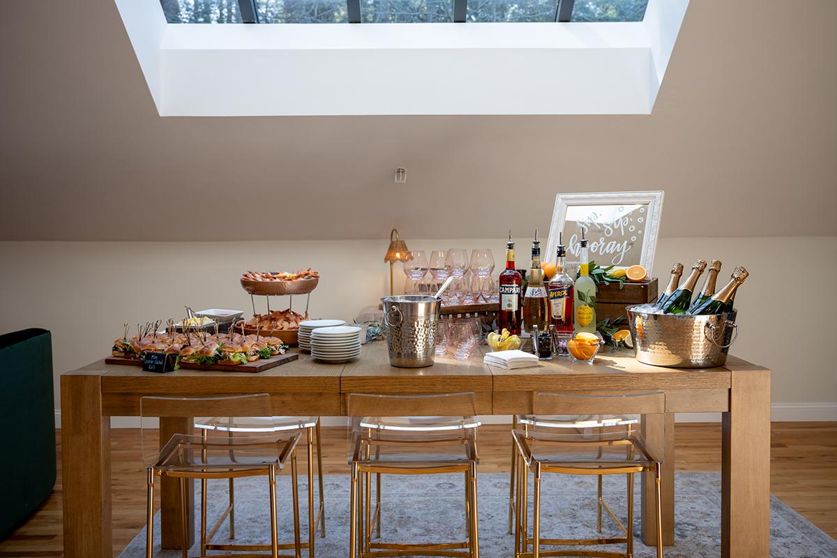 Buffet table with food, drinks, and champagne under a skylight.
