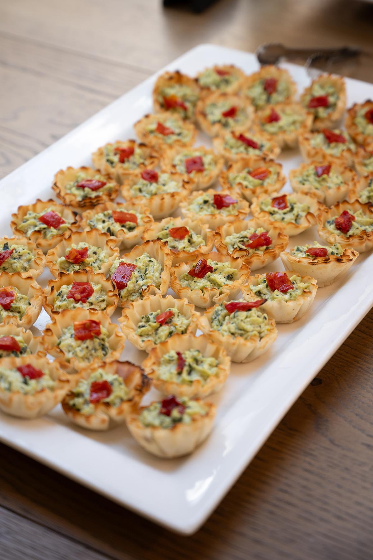 Mini quiches with vegetables and red garnish on a white platter.