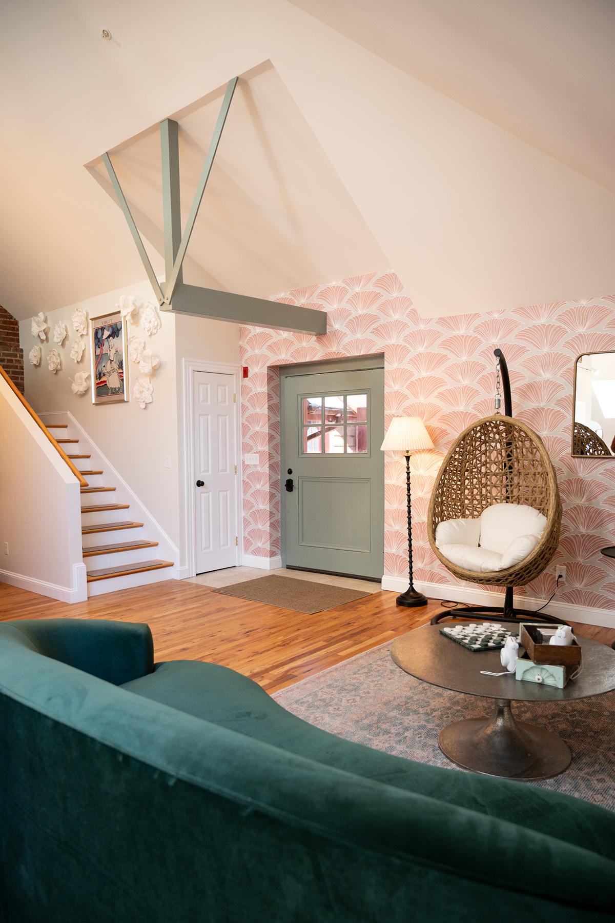 Cozy living room with green couch and hanging chair. Pink wallpaper and wooden floor.