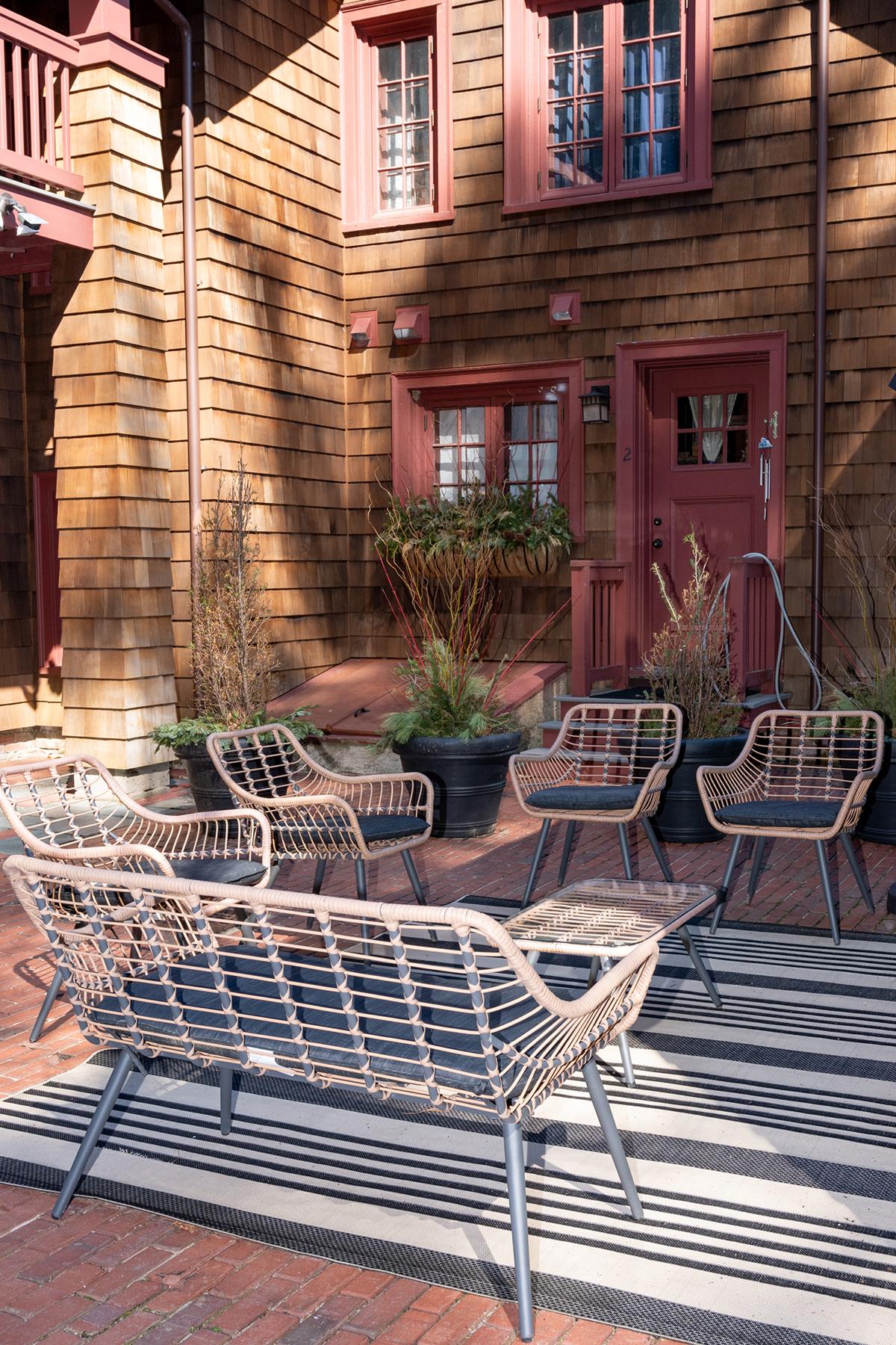 Wicker chairs on a patio with a wood-paneled house in the background.