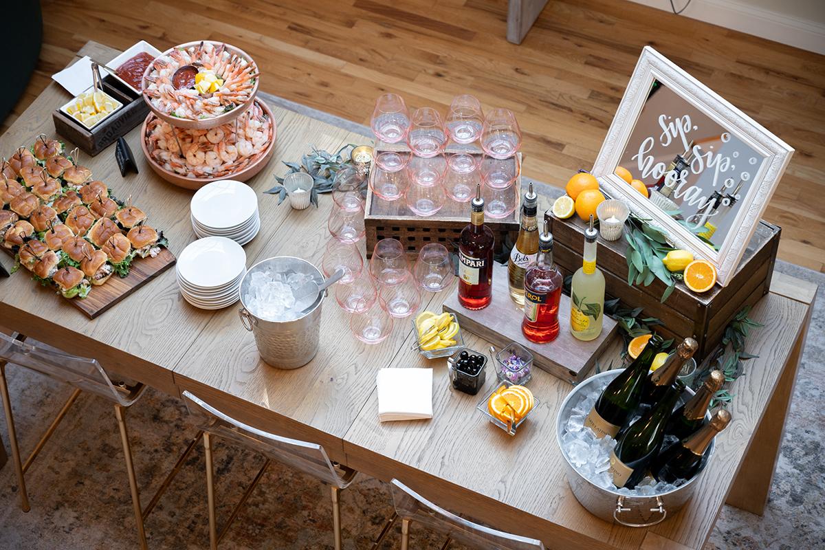 Buffet table with drinks, sandwiches, and fresh fruit.