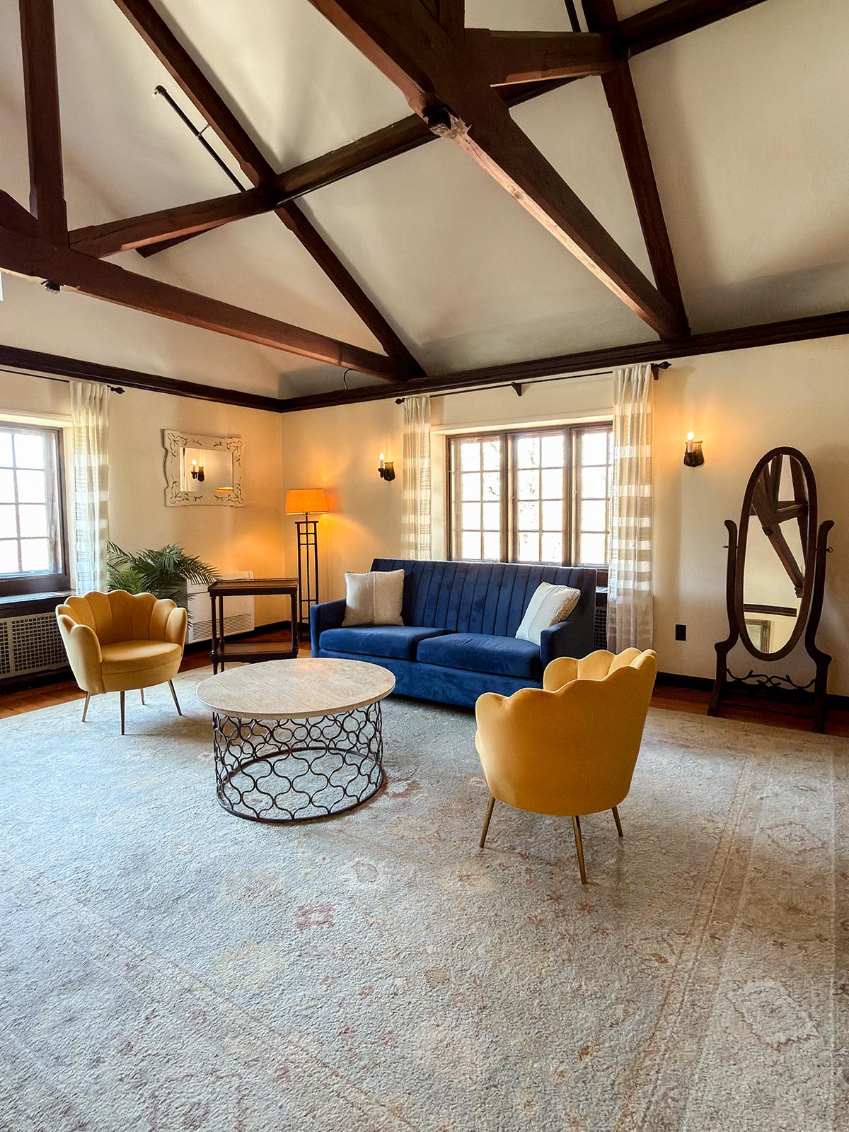 Cozy living room with blue sofa, yellow chairs, and oval mirror.