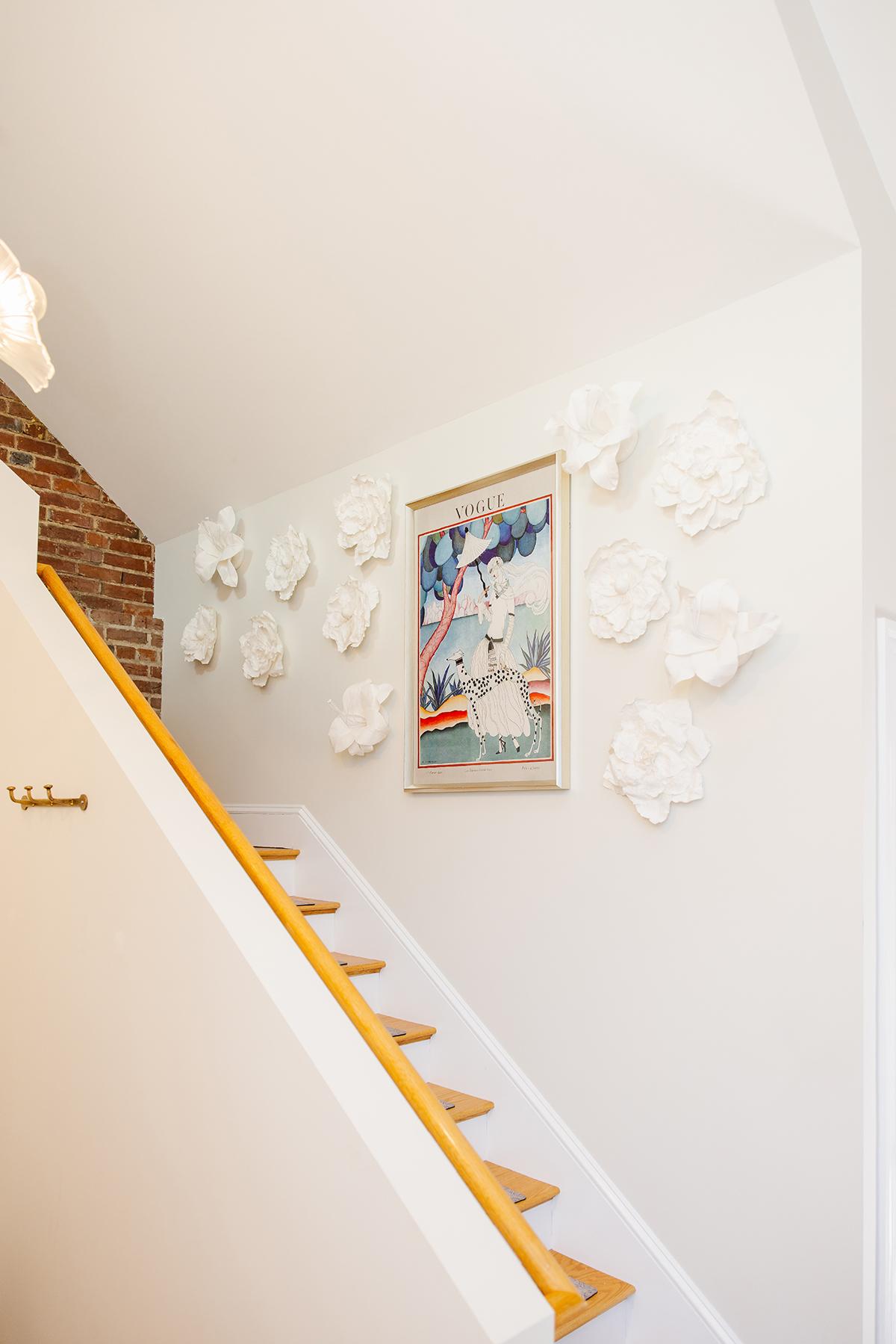 Stairway with white floral sculptures and framed artwork on the wall.