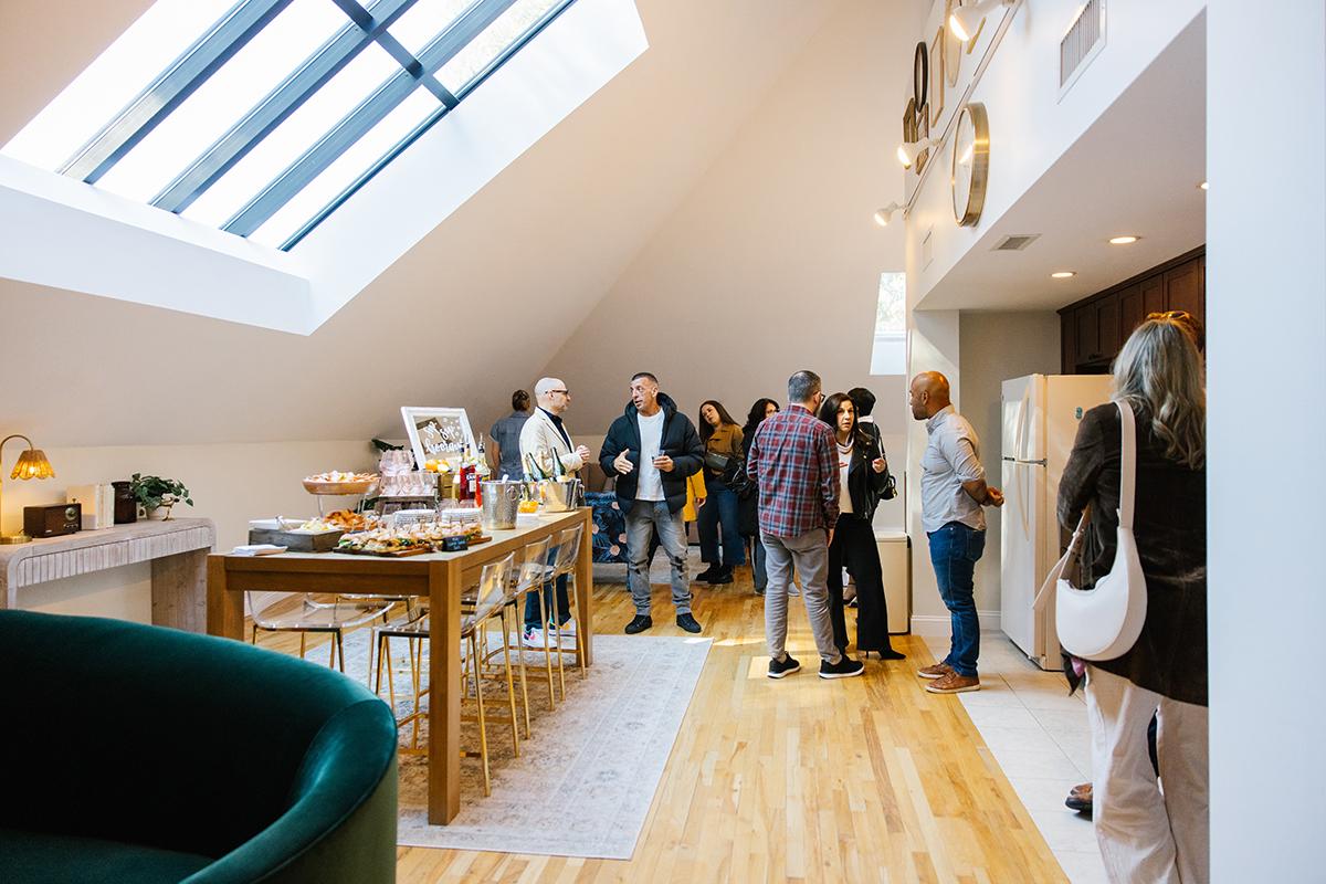 Bright loft gathering, people conversing around a dining table, skylight overhead.