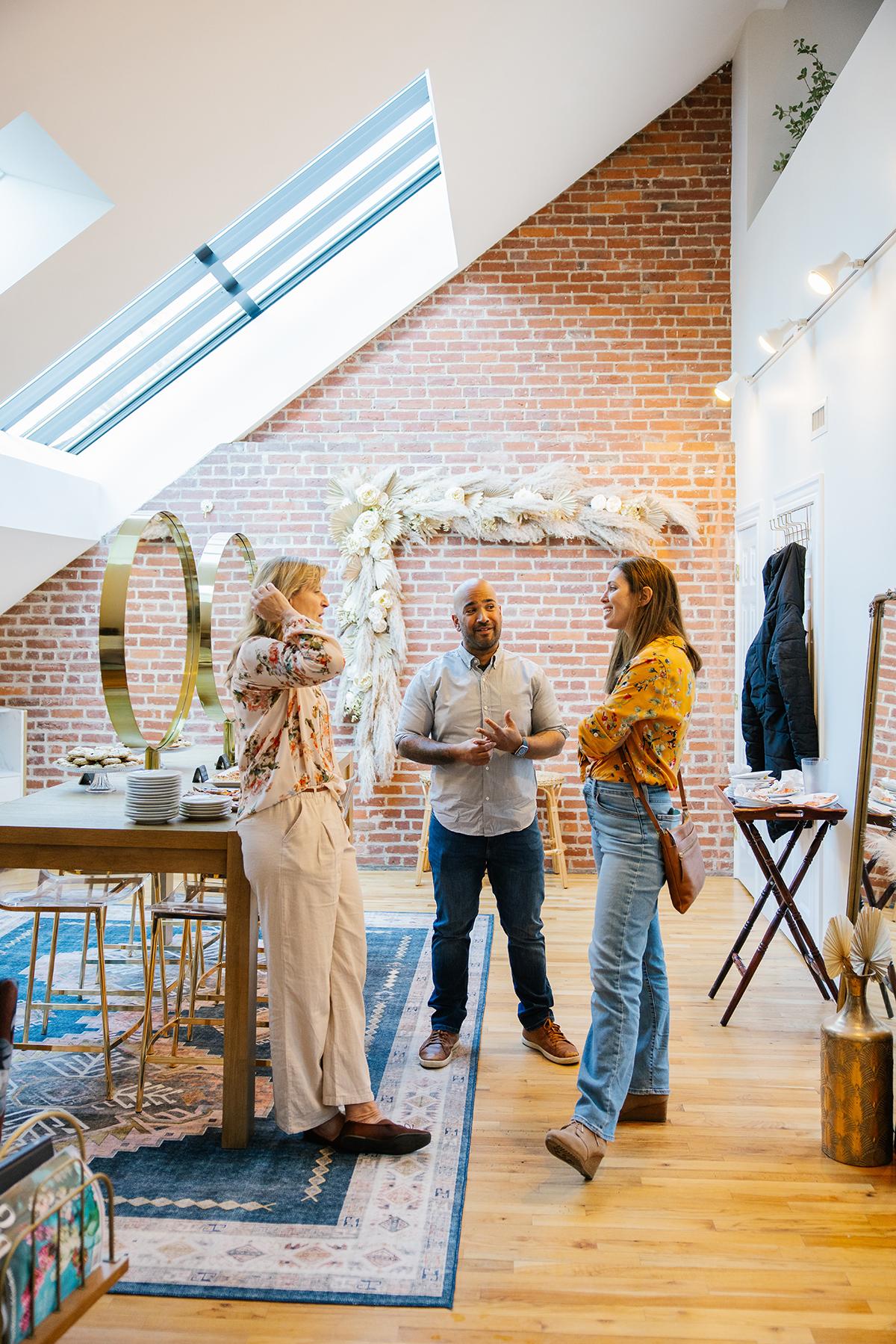 Three people chatting in a cozy loft with brick walls and a skylight.