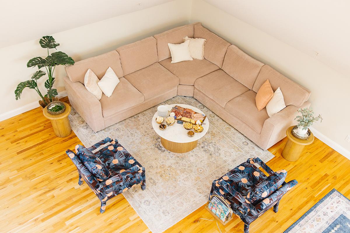 Beige sectional sofa, round coffee table, blue patterned chairs, and plants in a cozy living room.