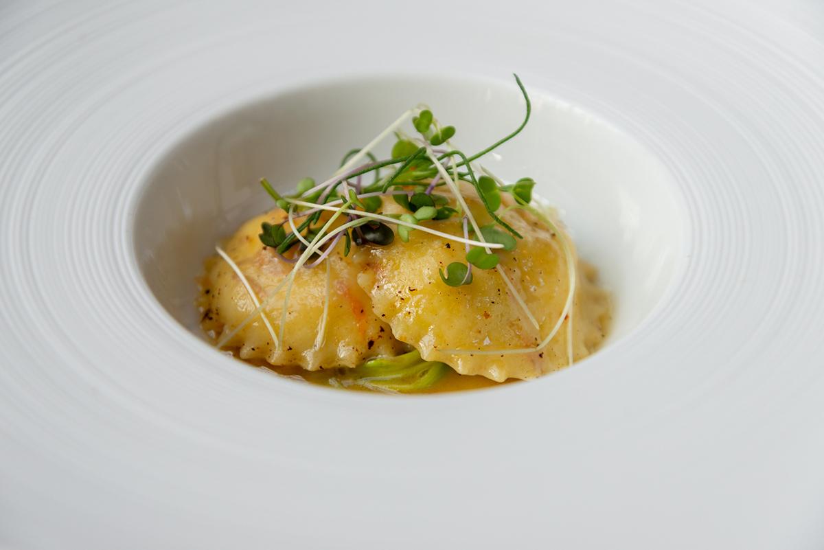 Ravioli topped with sprouts in a white bowl.