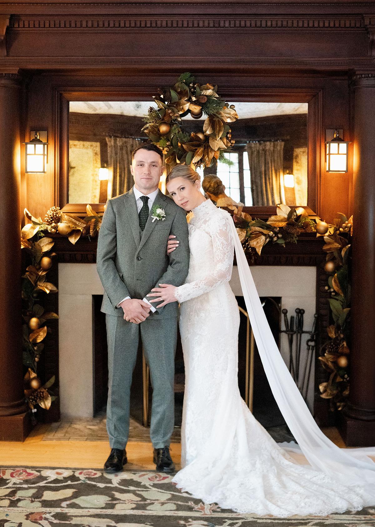 Bride and groom in front of a decorated fireplace, embracing warmly.
