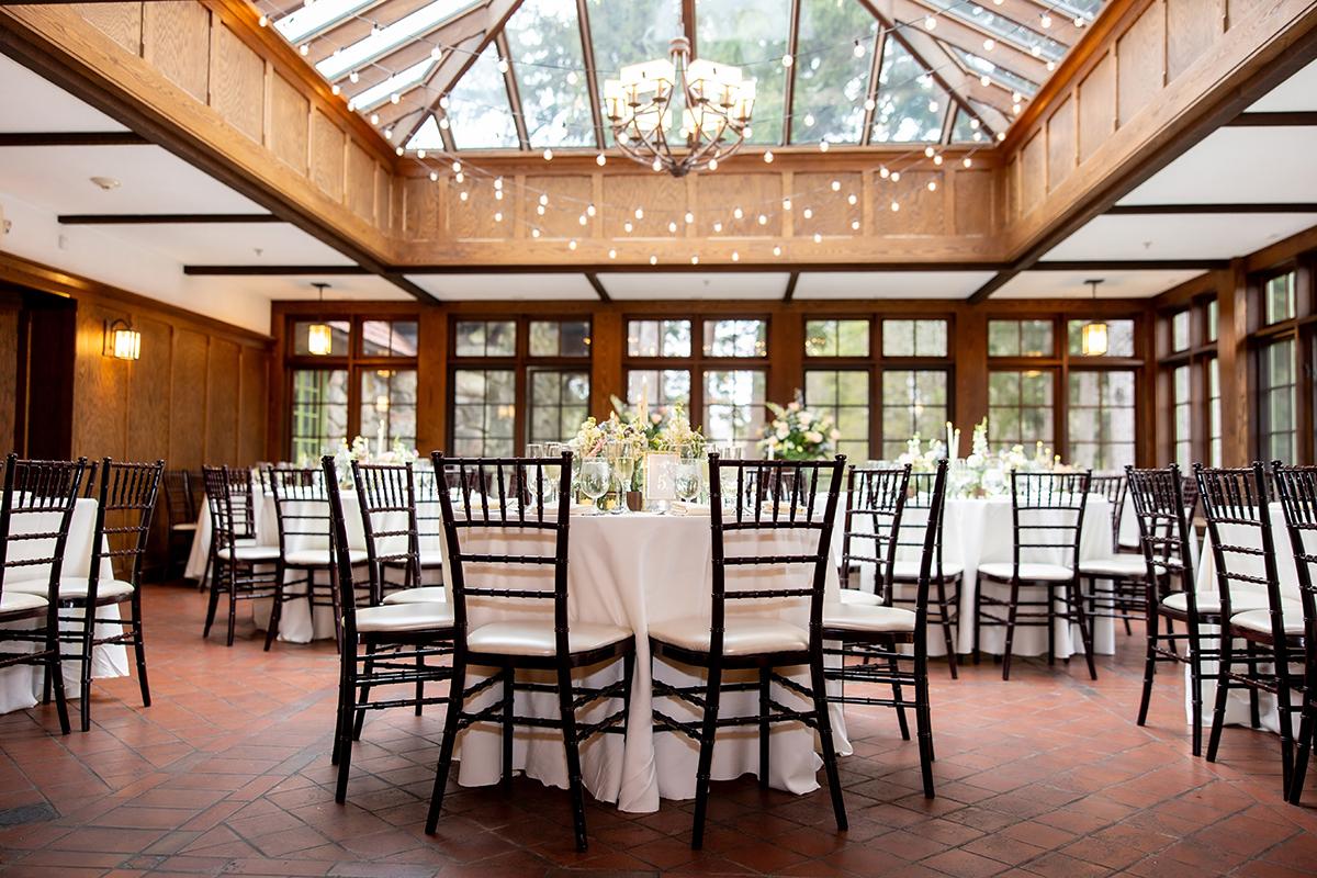 Elegant banquet hall with round tables, white tablecloths, dark chairs, and a glass ceiling.