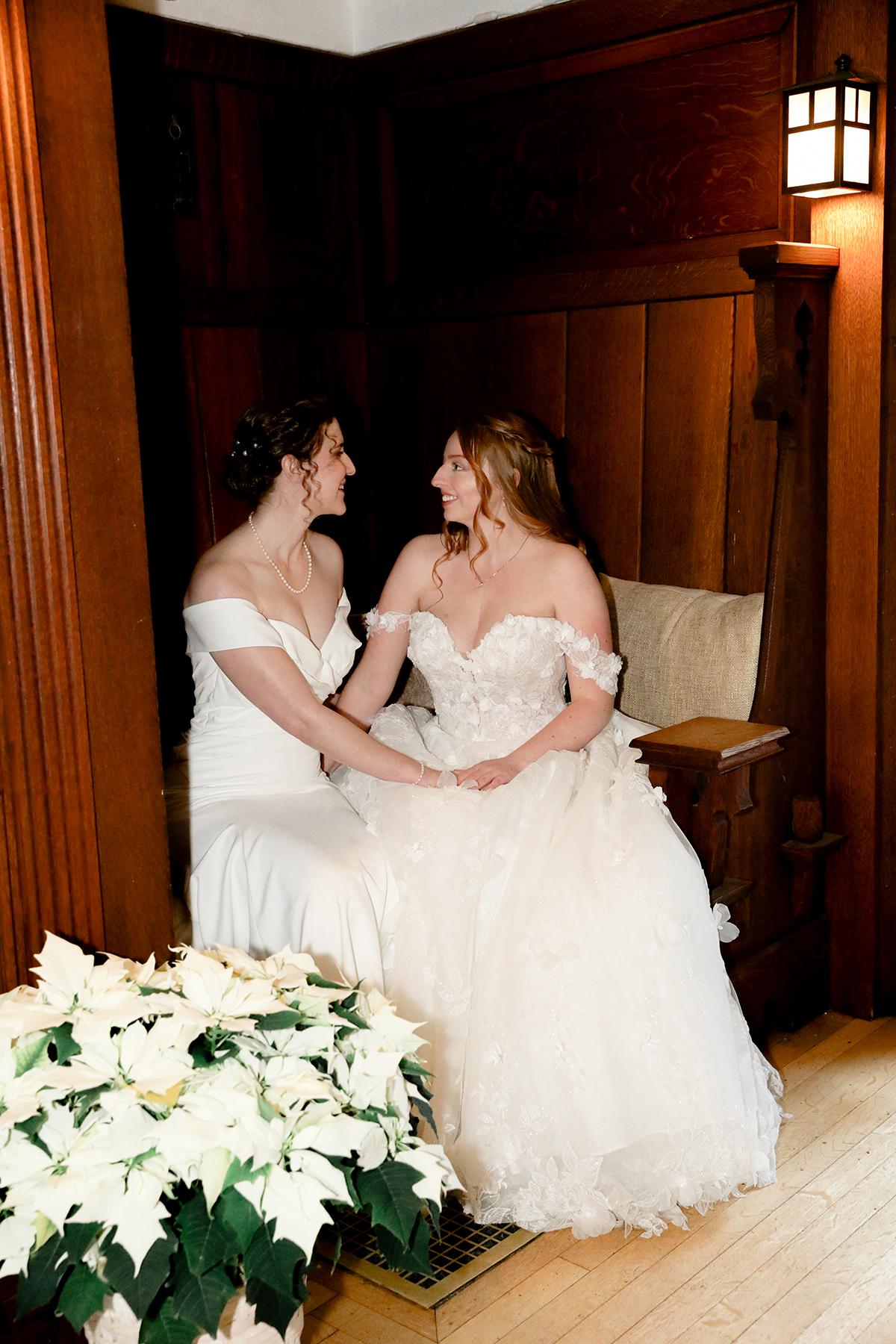 Two brides in white dresses sitting together, smiling fondly.