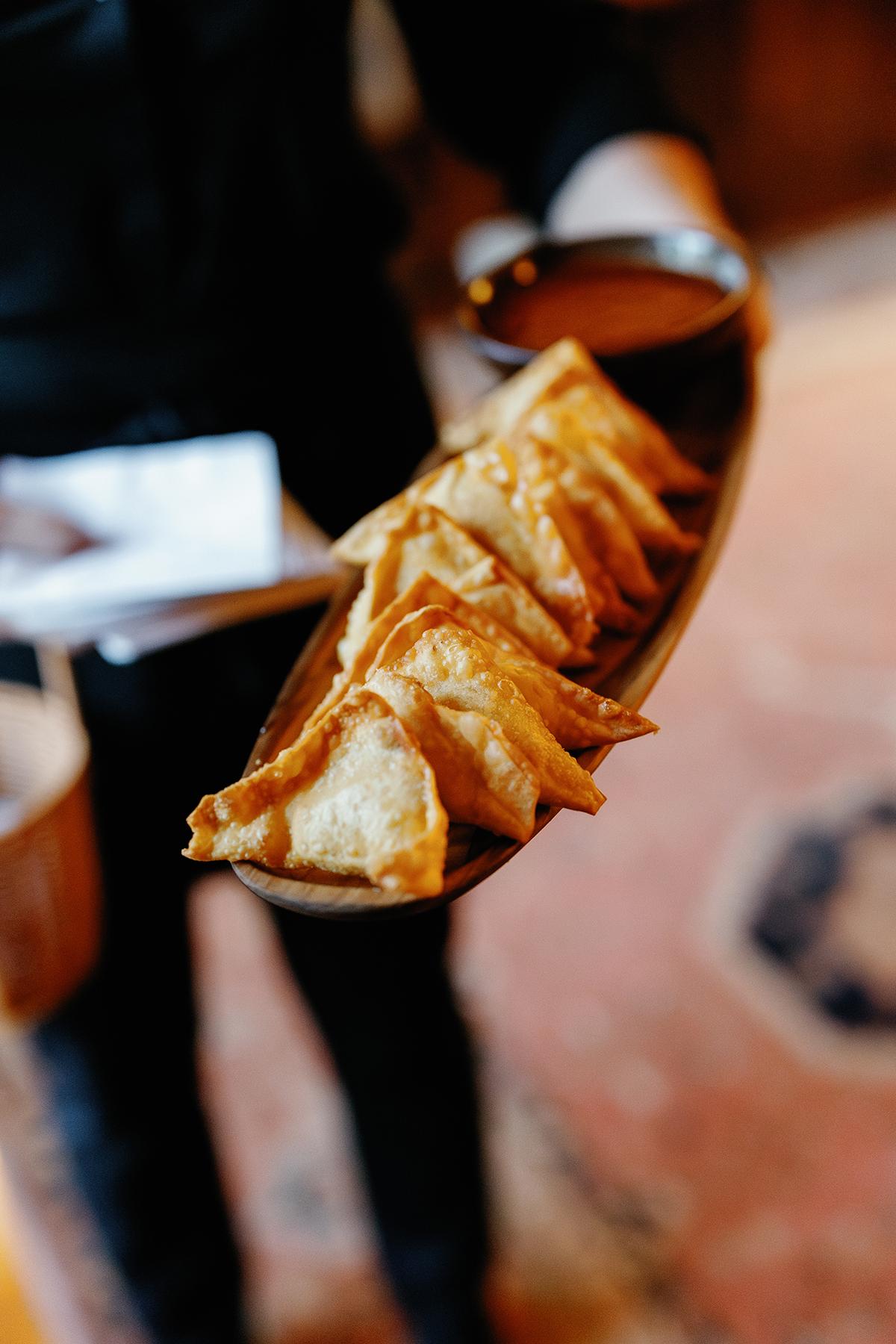 Golden fried dumplings on a long plate, with a bowl of sauce.