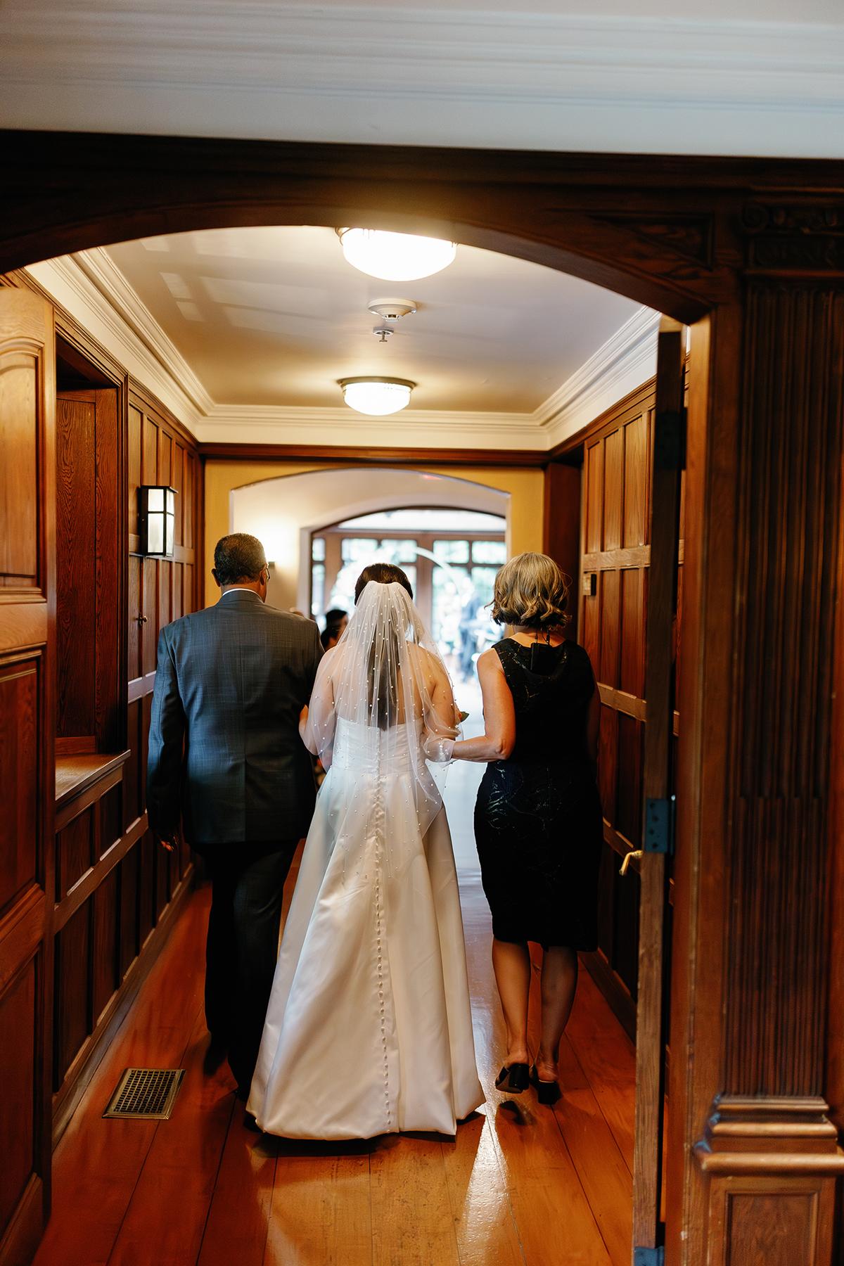 Three people walking down a hallway, one in a wedding dress.