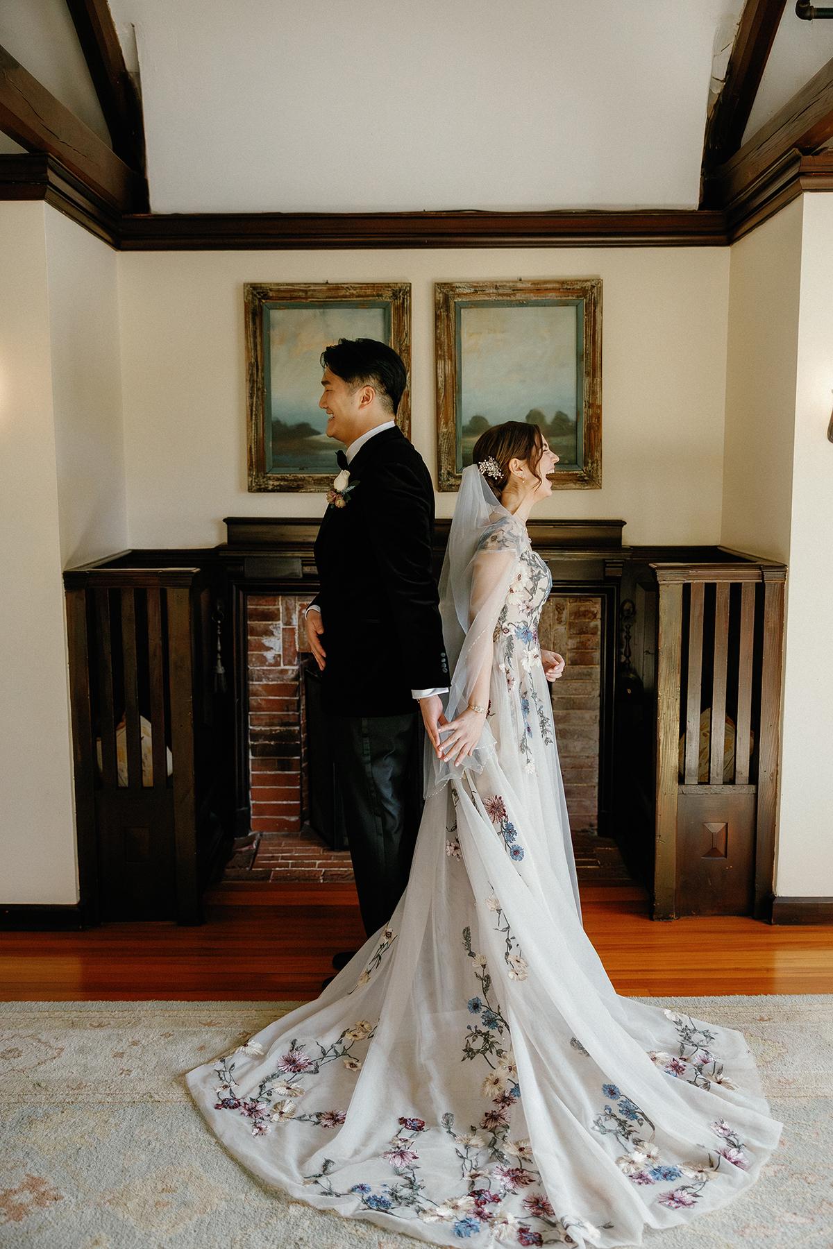 Bride and groom stand back-to-back in an elegant room.