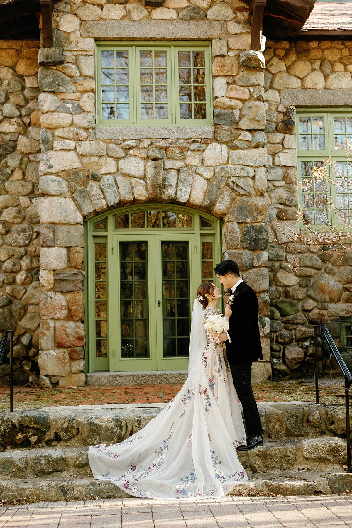 Bride and groom embrace on stone building steps, soft sunlight.