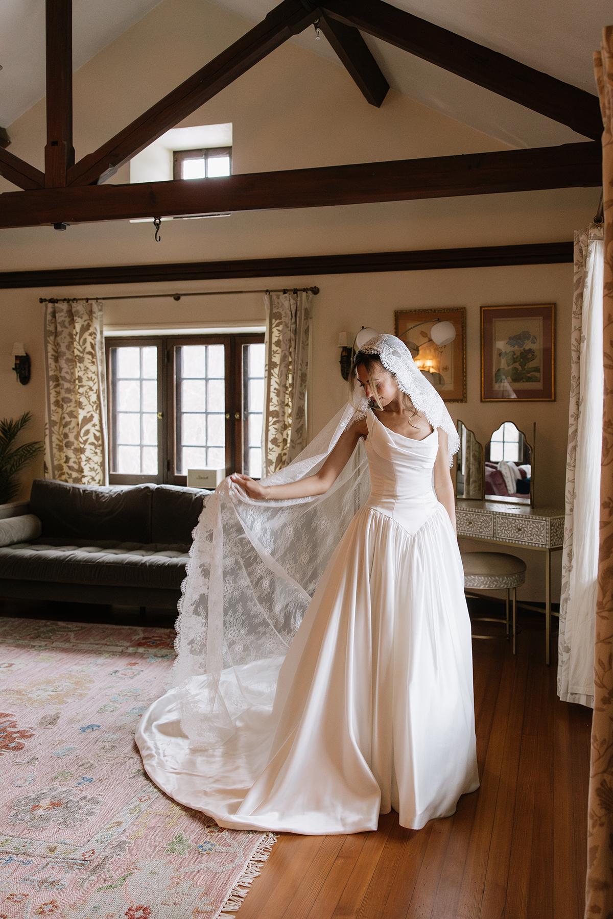 Bride in a white dress with veil, standing in a cozy living room.