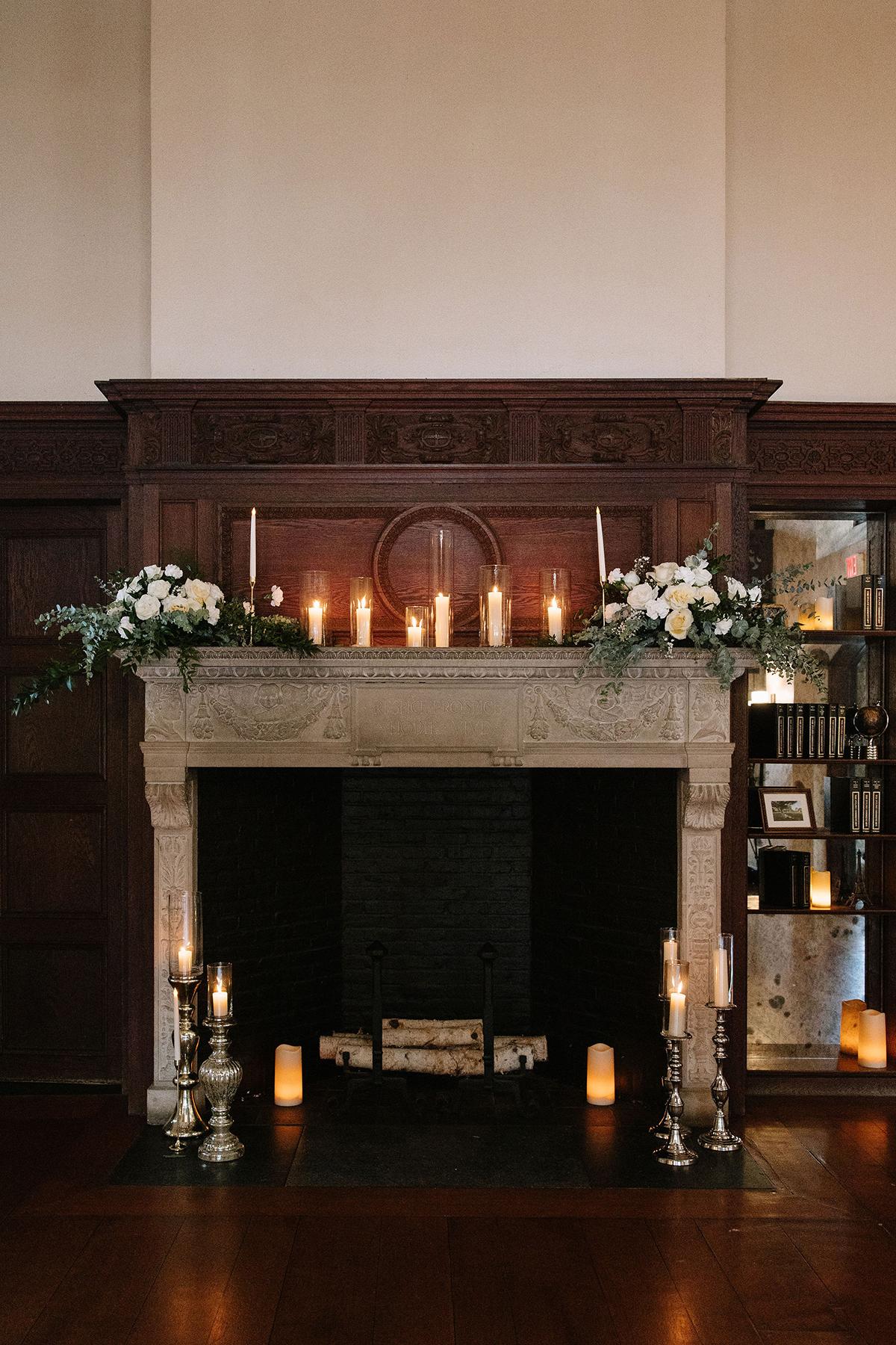 Elegant fireplace with candles, white flowers, and wooden paneling.