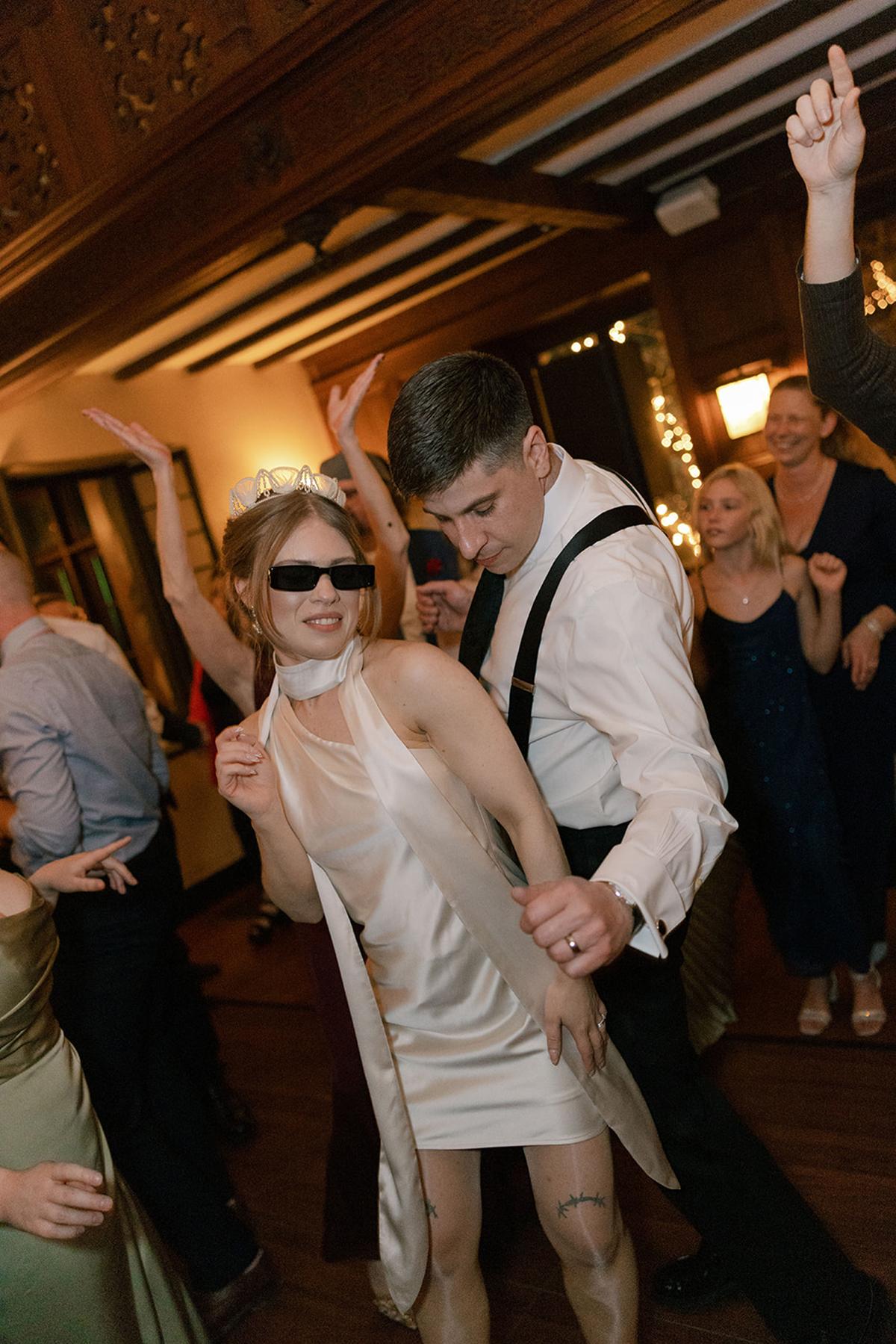 Couple dancing energetically at a party, wearing formal attire.