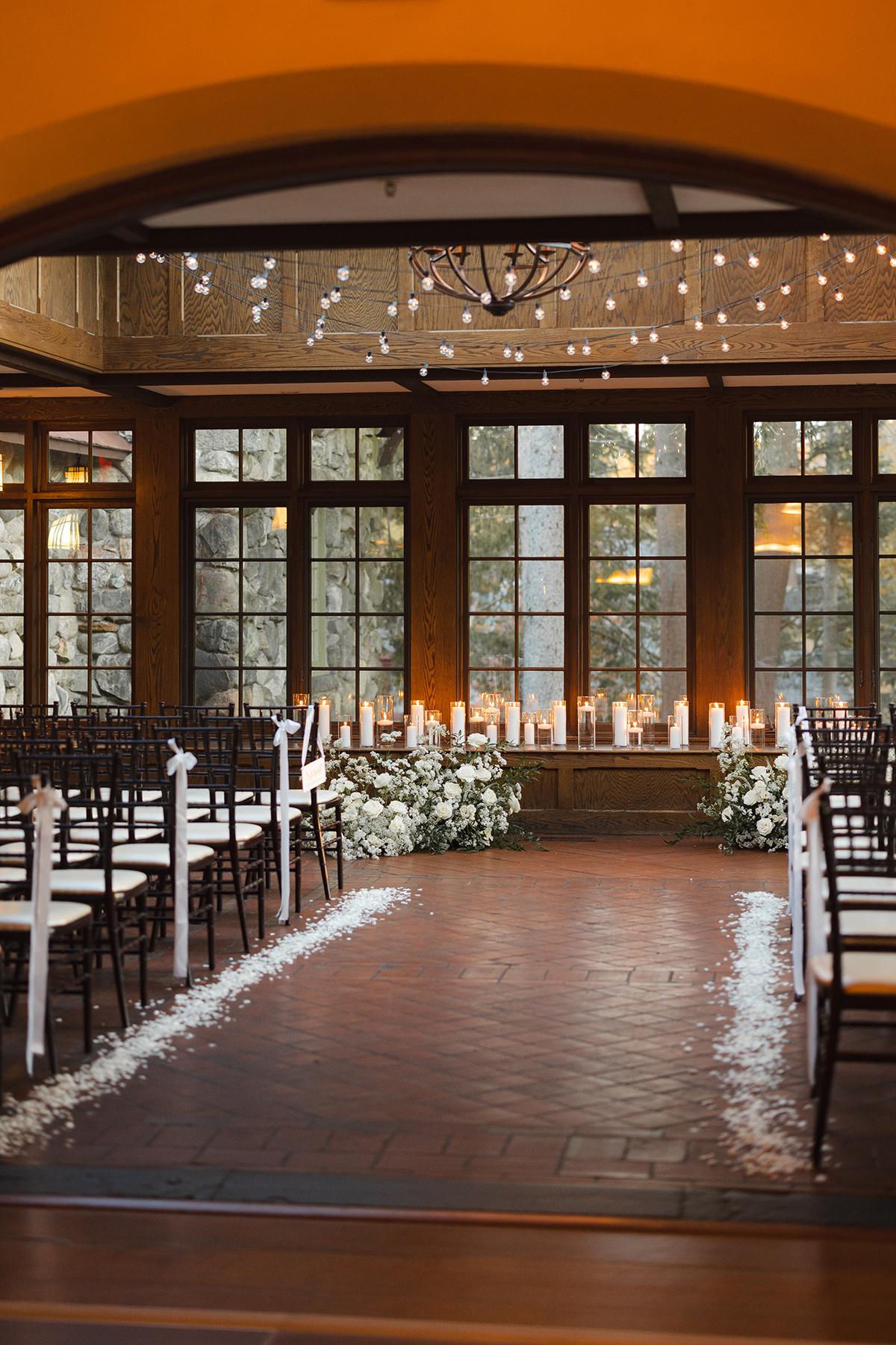 Elegant wedding aisle with candles and white flowers in a warmly lit room.