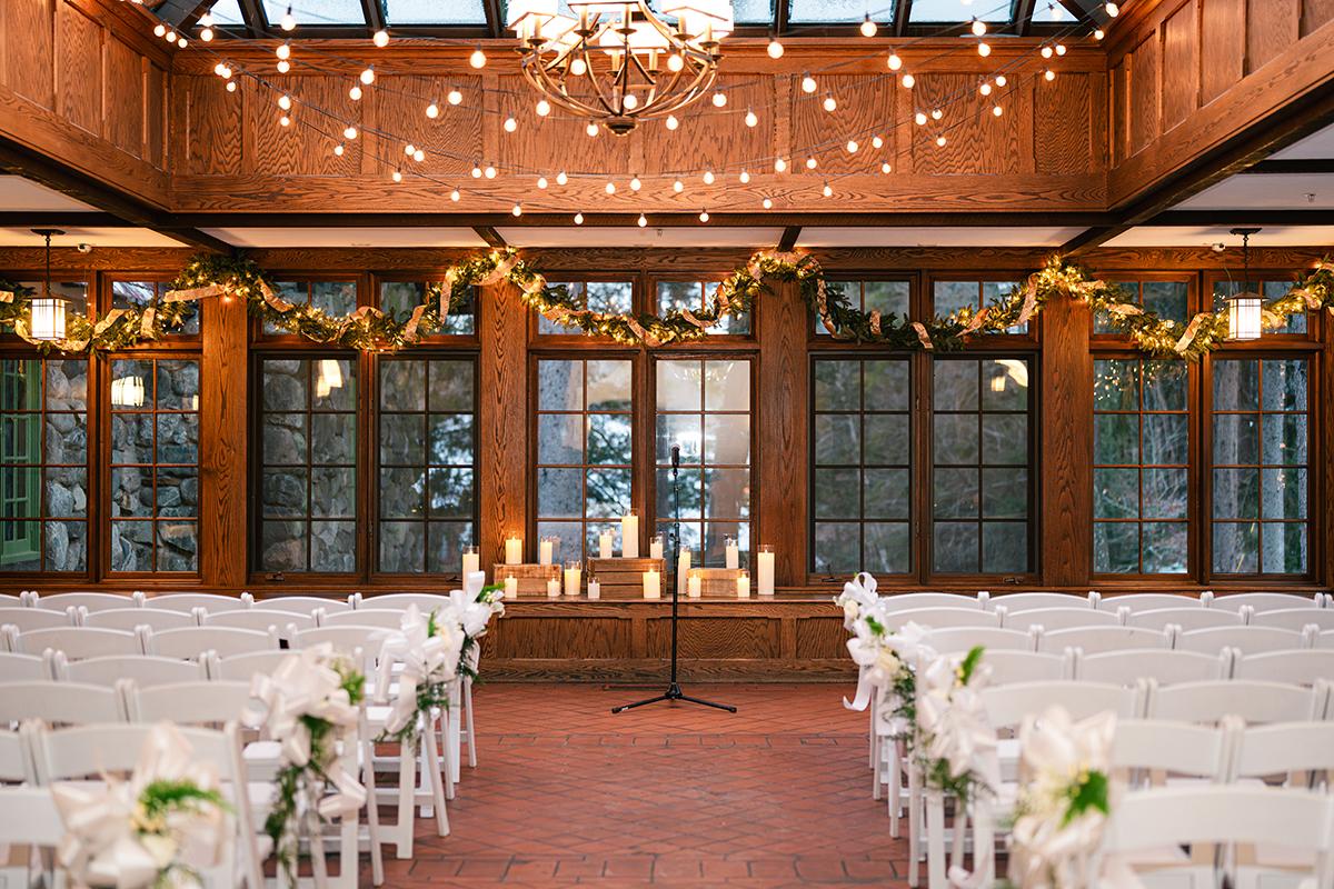 Wedding ceremony setup in a rustic hall with white chairs and candle-lit altar.