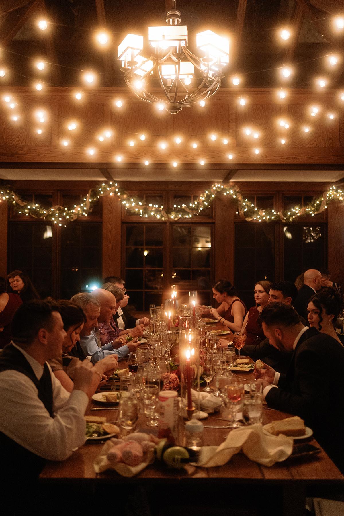 Warmly lit banquet with people dining under string lights.