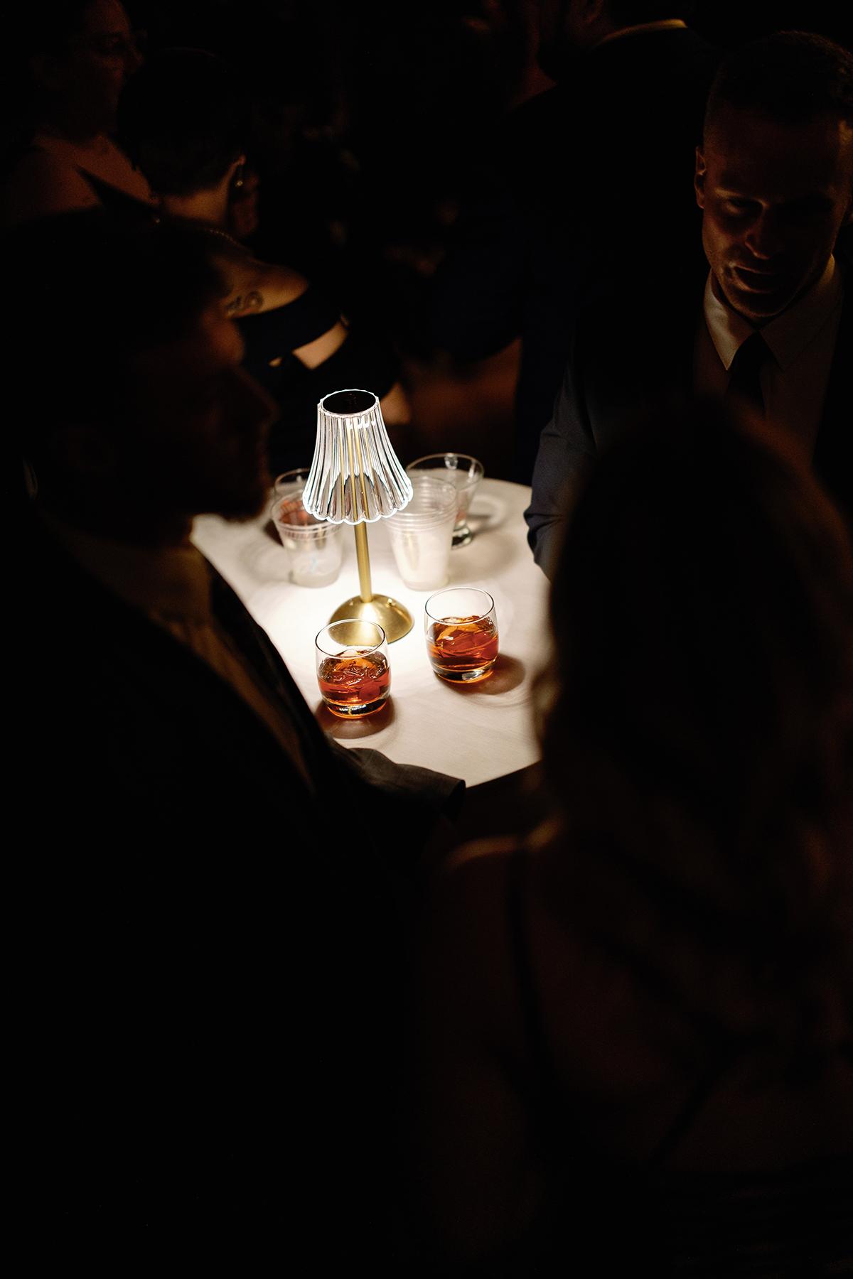 Dimly lit table with drinks and people in evening attire.