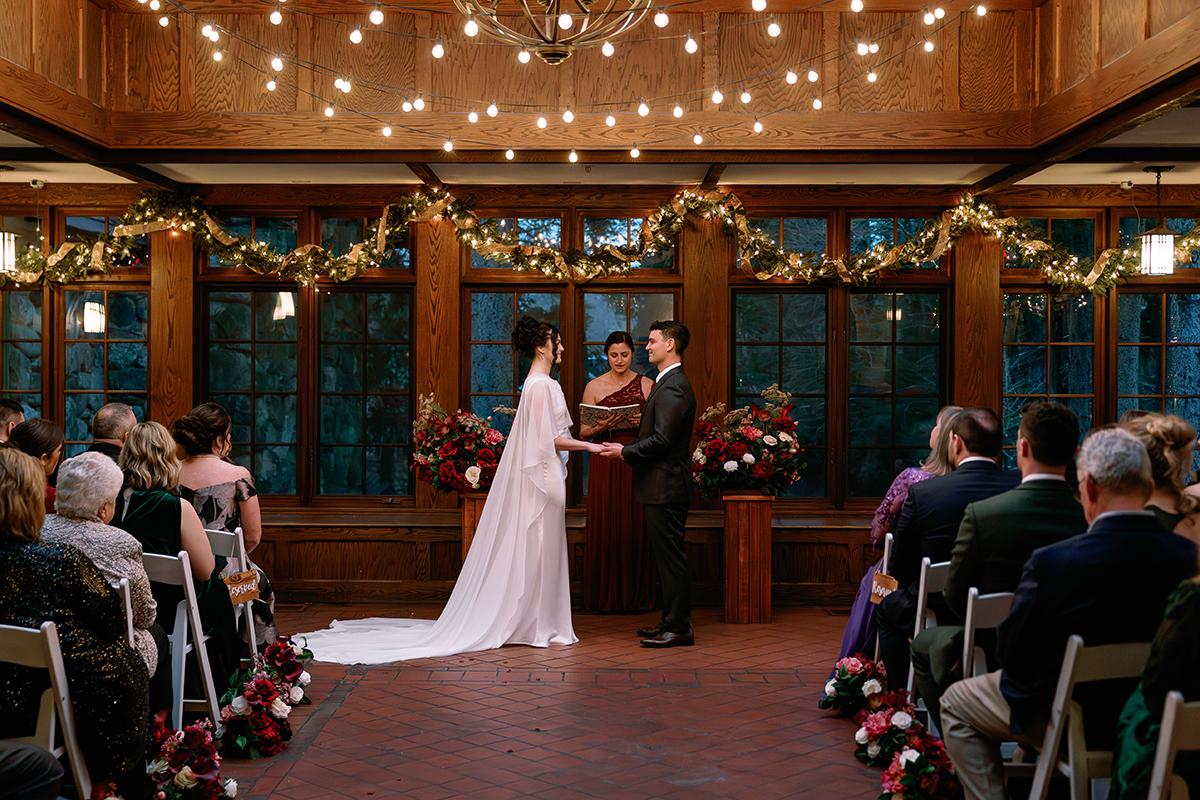 Wedding ceremony in a warmly lit wooden hall with guests seated.
