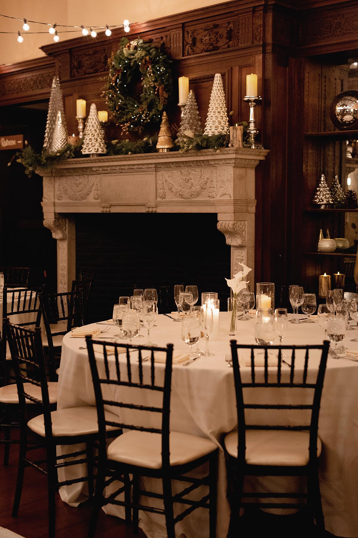 Elegant dining setting with candlelit table and festive mantel decor.