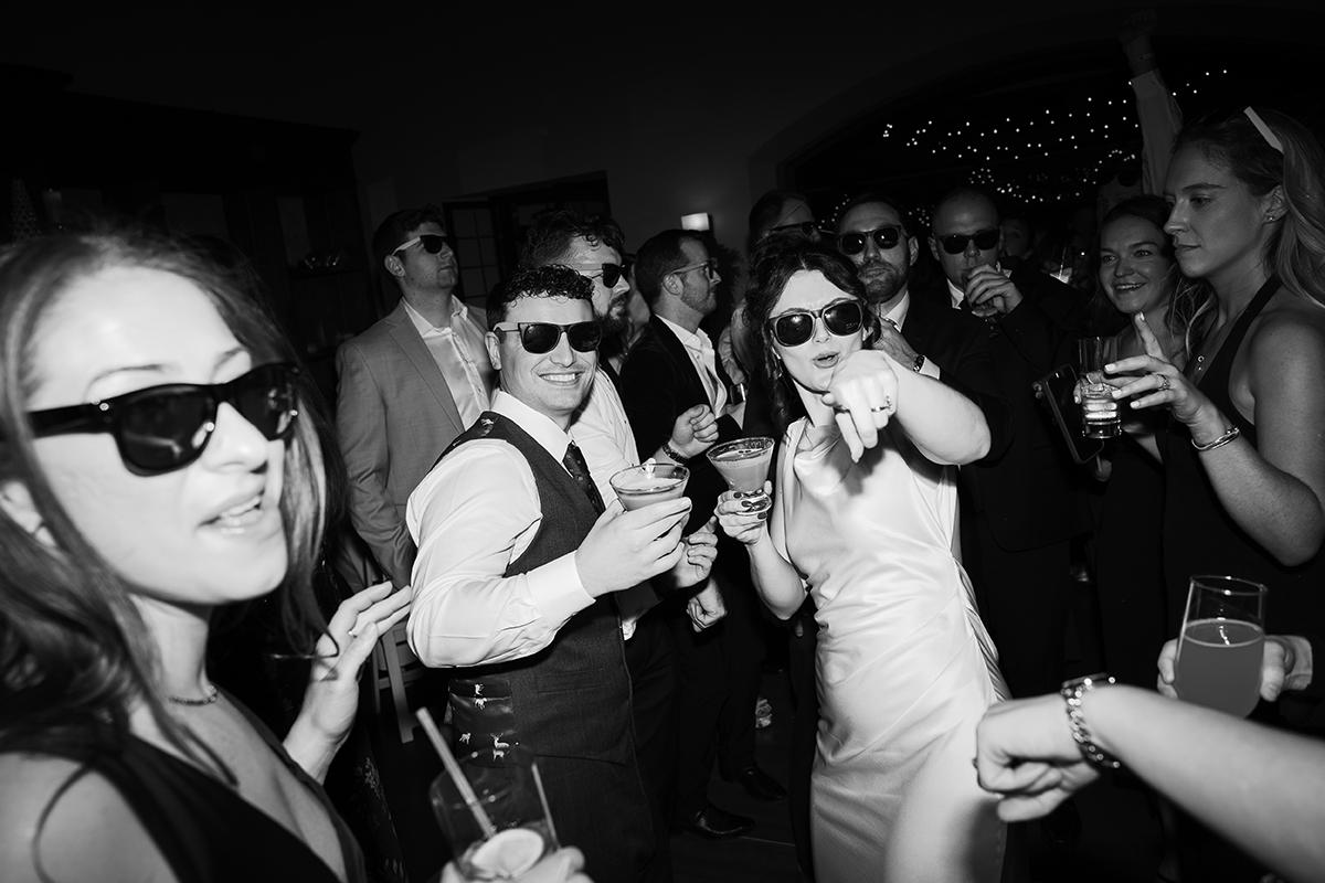 Black and white photo of people dancing and wearing sunglasses at a party.