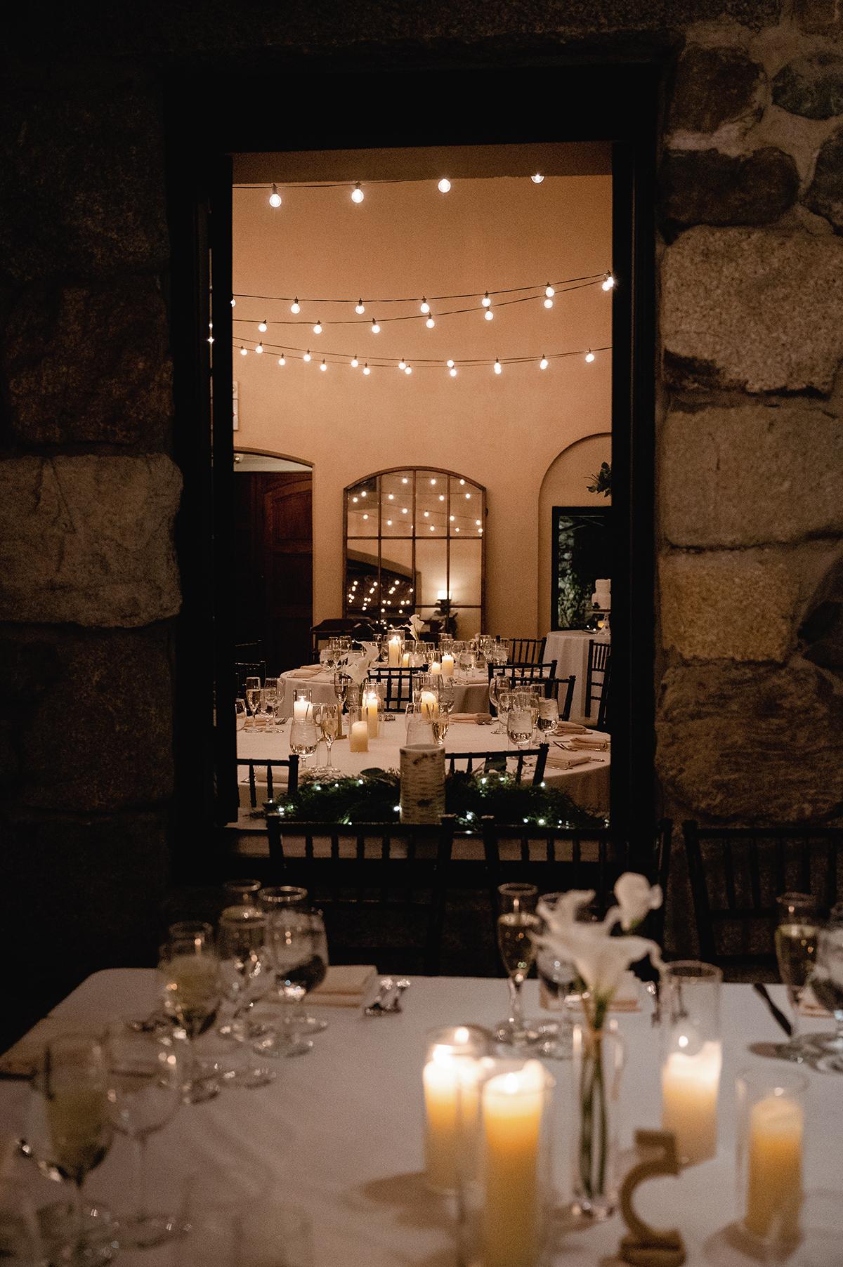Candlelit dinner setting seen through a window, with string lights above.