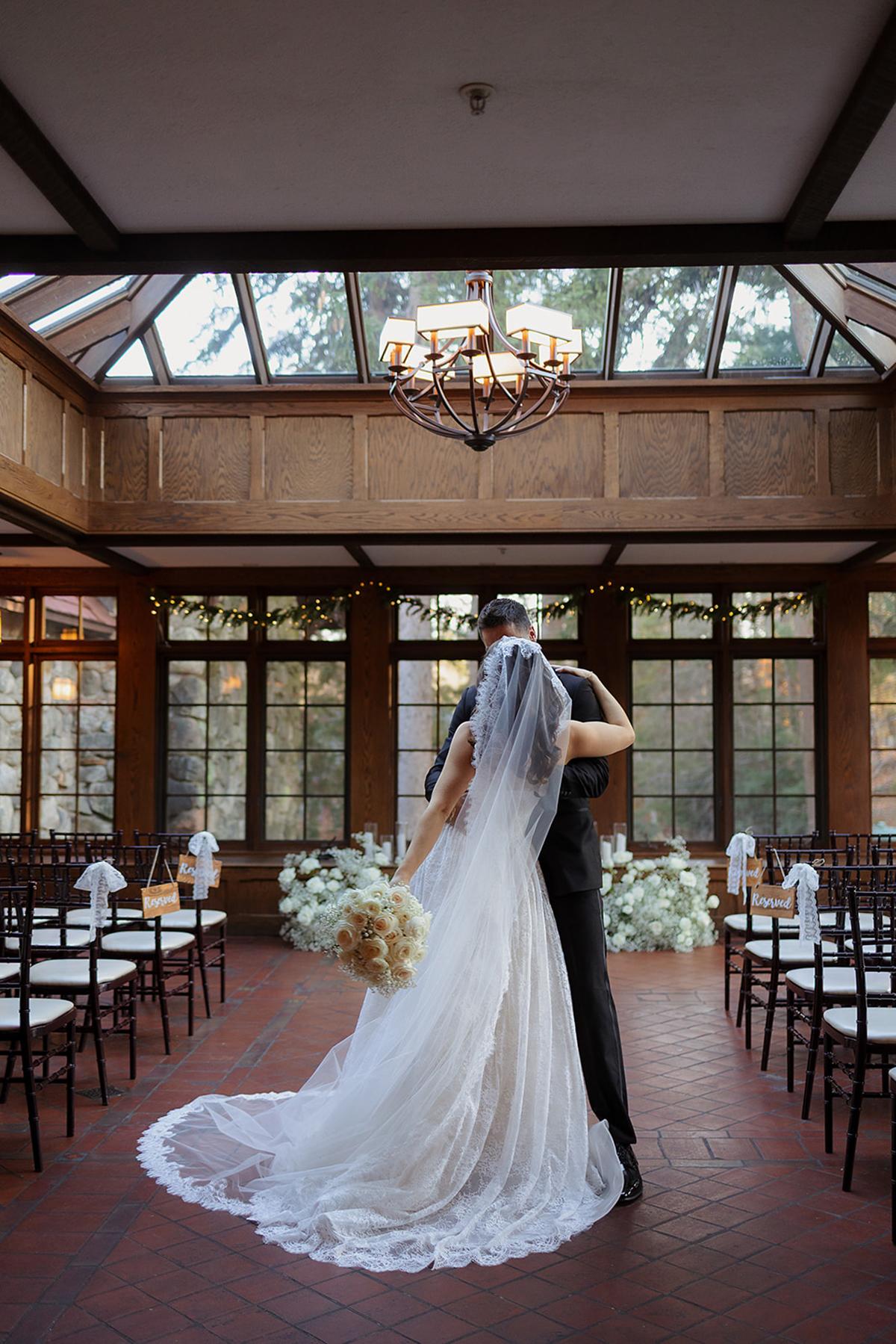 Bride and groom embrace in a sunlit hall with a glass ceiling.