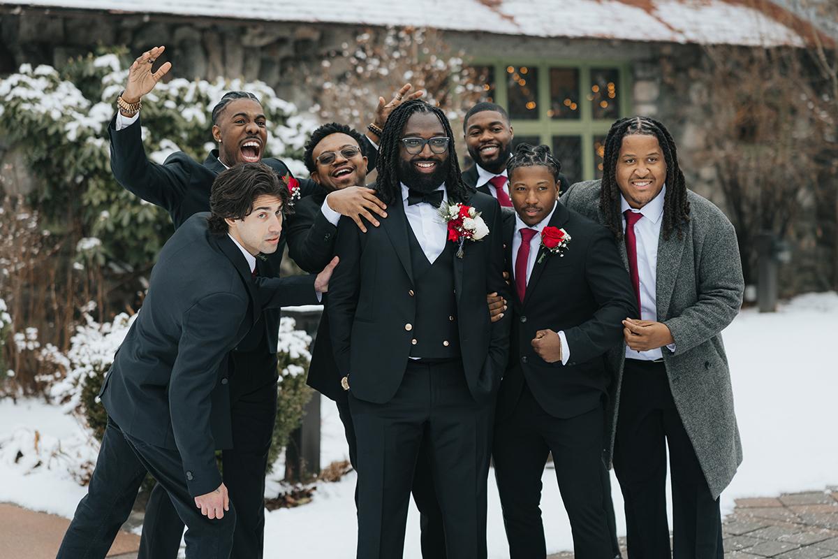 Groomsmen in suits smiling in snowy outdoor setting.
