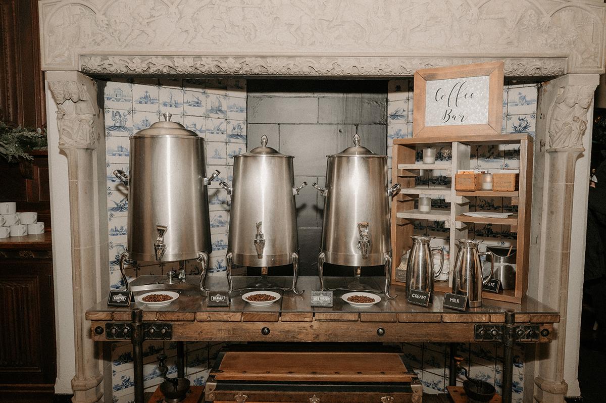 Buffet with three large silver urns for hot beverages on a wooden table.