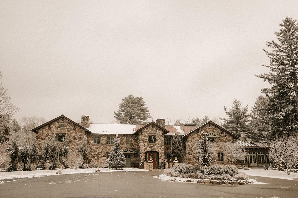 Stone house surrounded by snow-covered trees under an overcast sky.