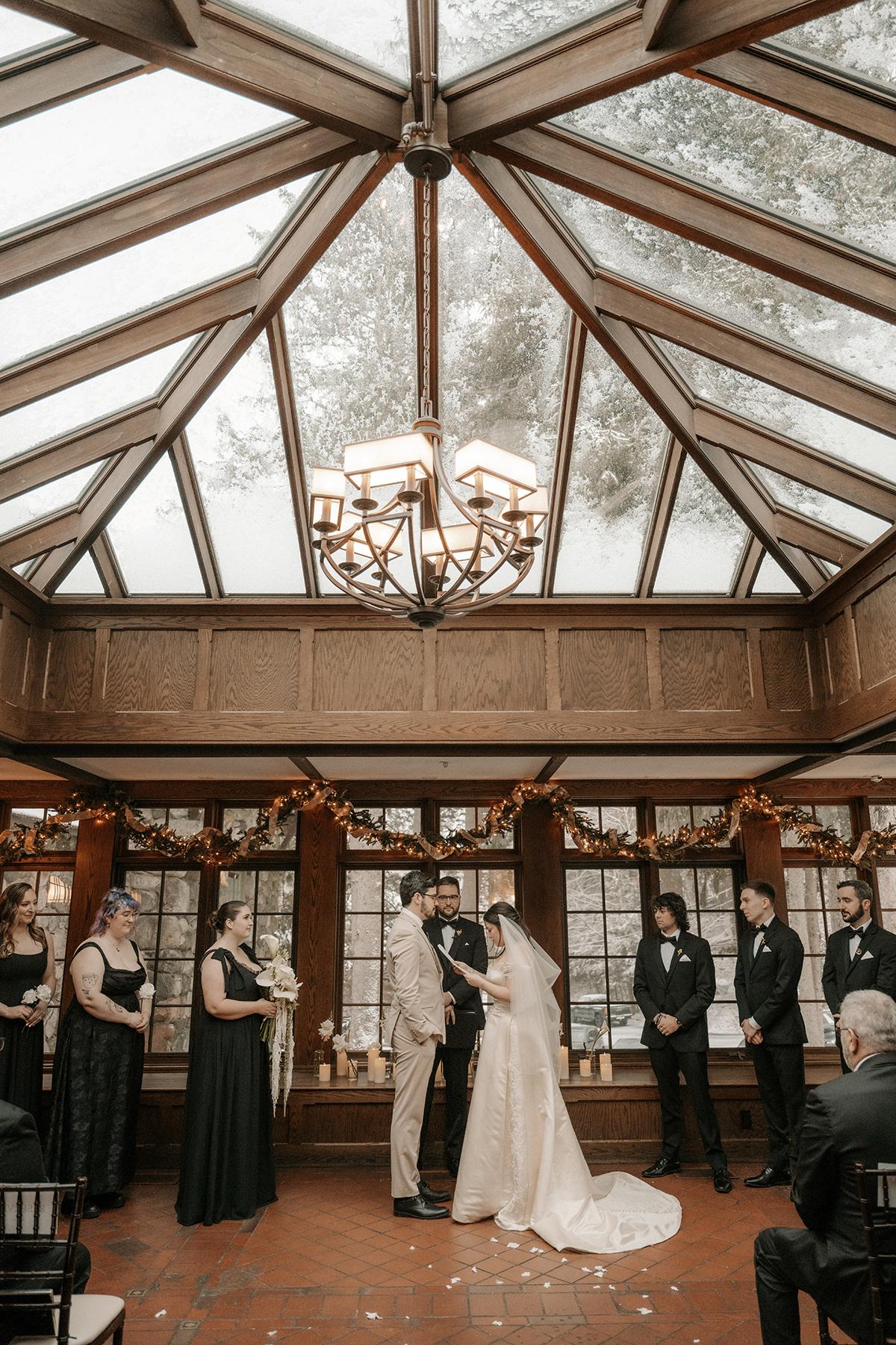 Bride and groom under a glass ceiling, surrounded by bridesmaids and groomsmen.