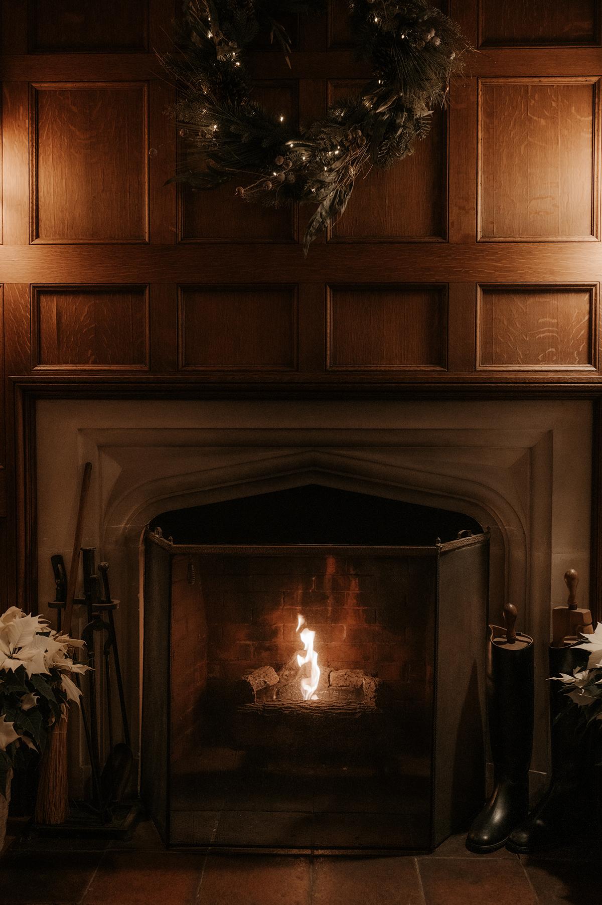 Cozy fireplace with a wreath above and boots beside it.
