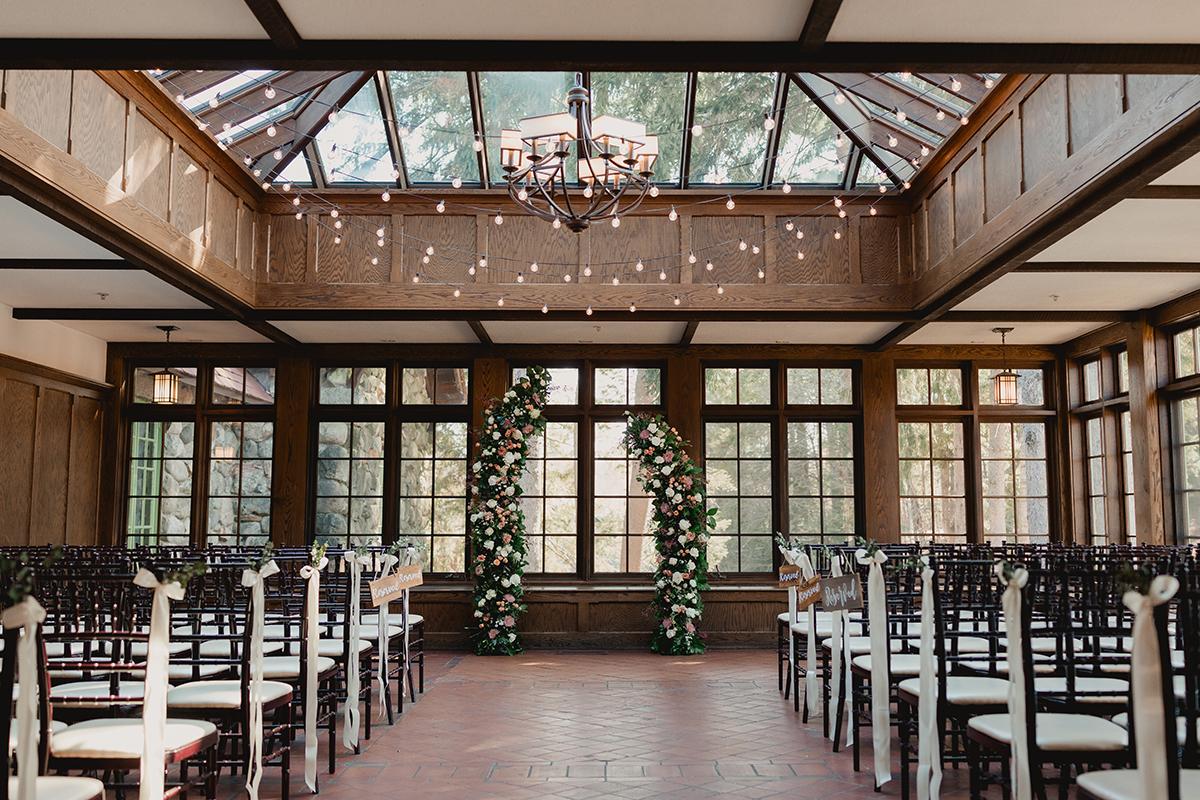Wedding venue with wooden interior and floral decorations. Rows of chairs line the aisle.