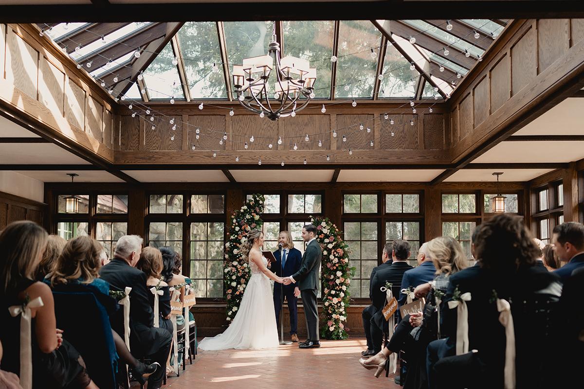 Wedding ceremony in a sunlit, wooden venue with guests seated and a couple at the altar.