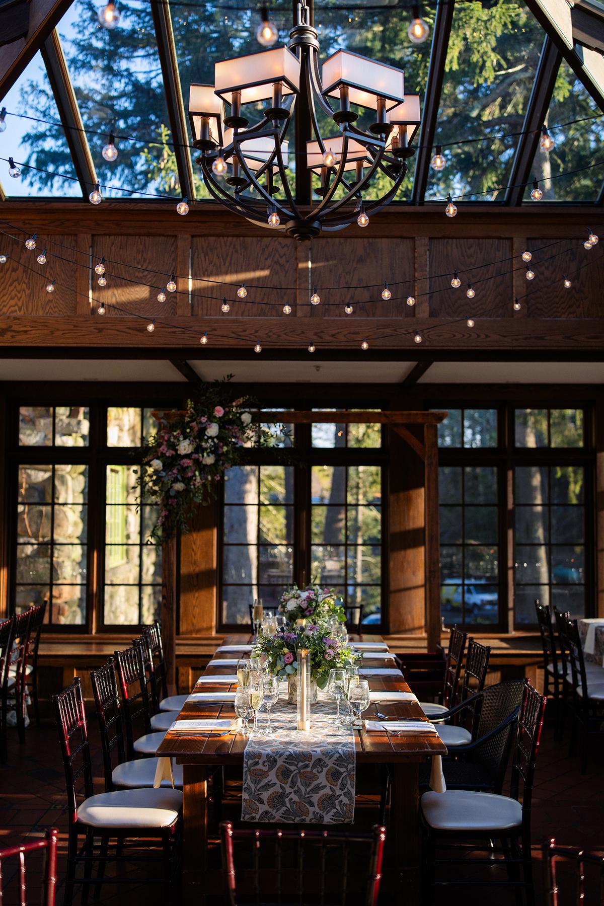 Elegant dining table under a glass ceiling with chandeliers and floral centerpiece.