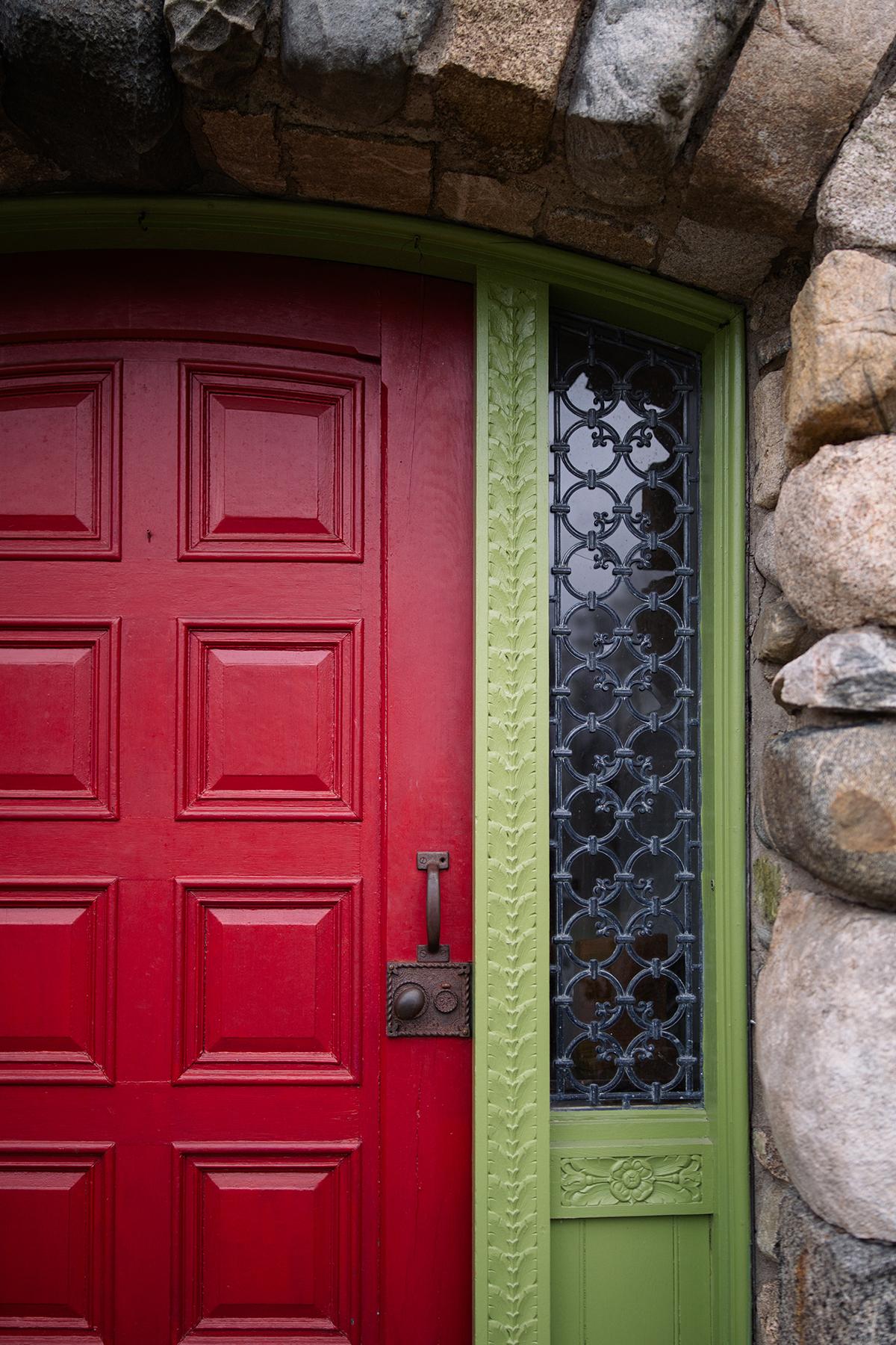 Red wooden door with ornate metal window set in a stone arch frame.