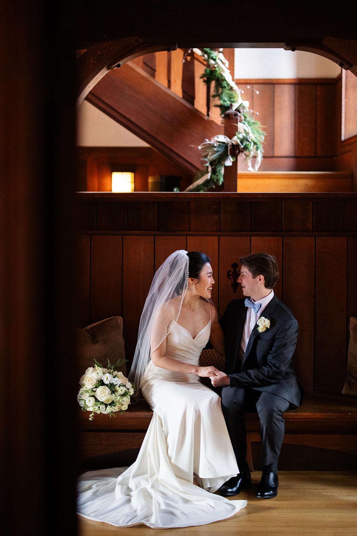 Bride and groom sitting inside, smiling at each other.