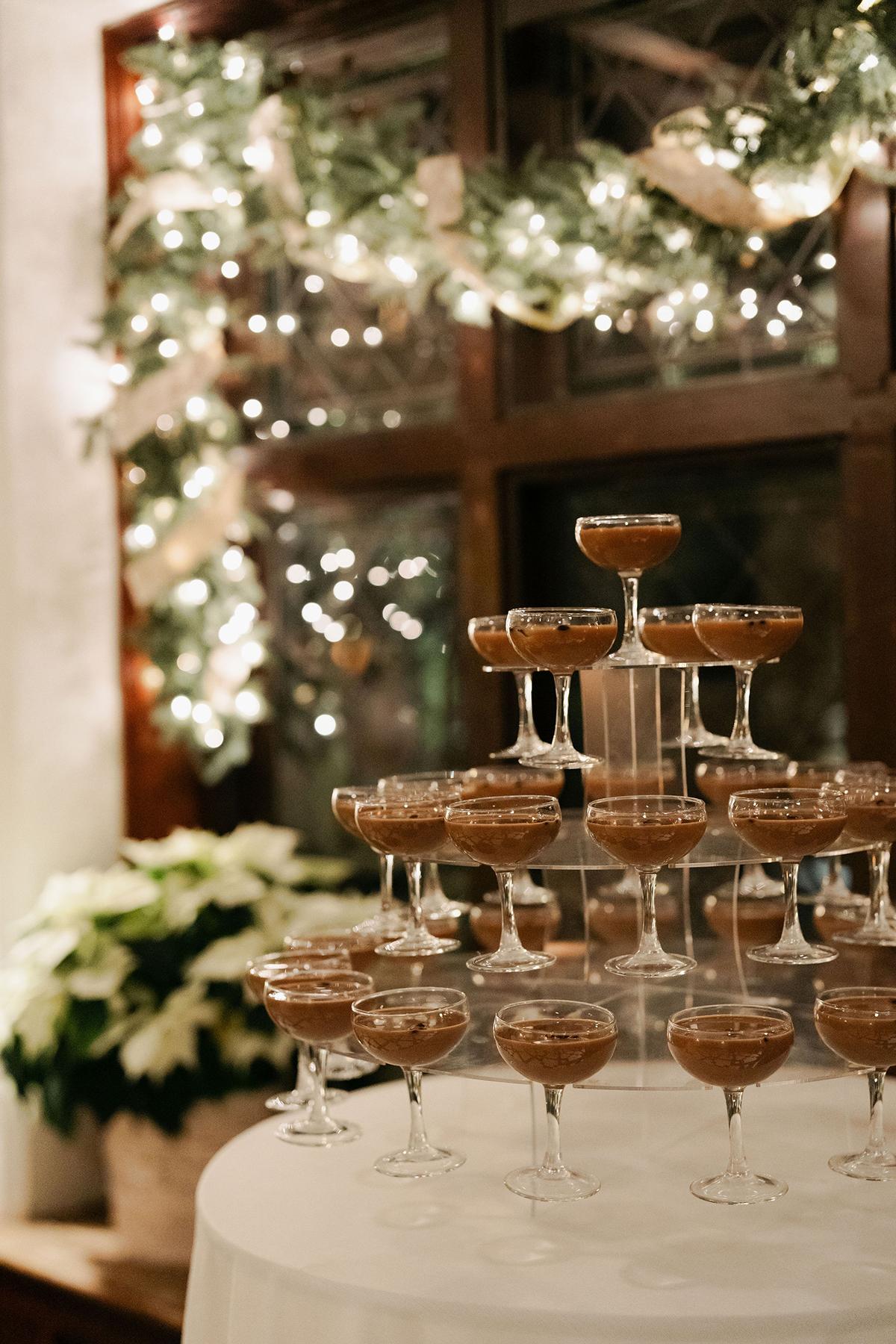Champagne coupes and dessert glasses on a table before a lit Christmas tree