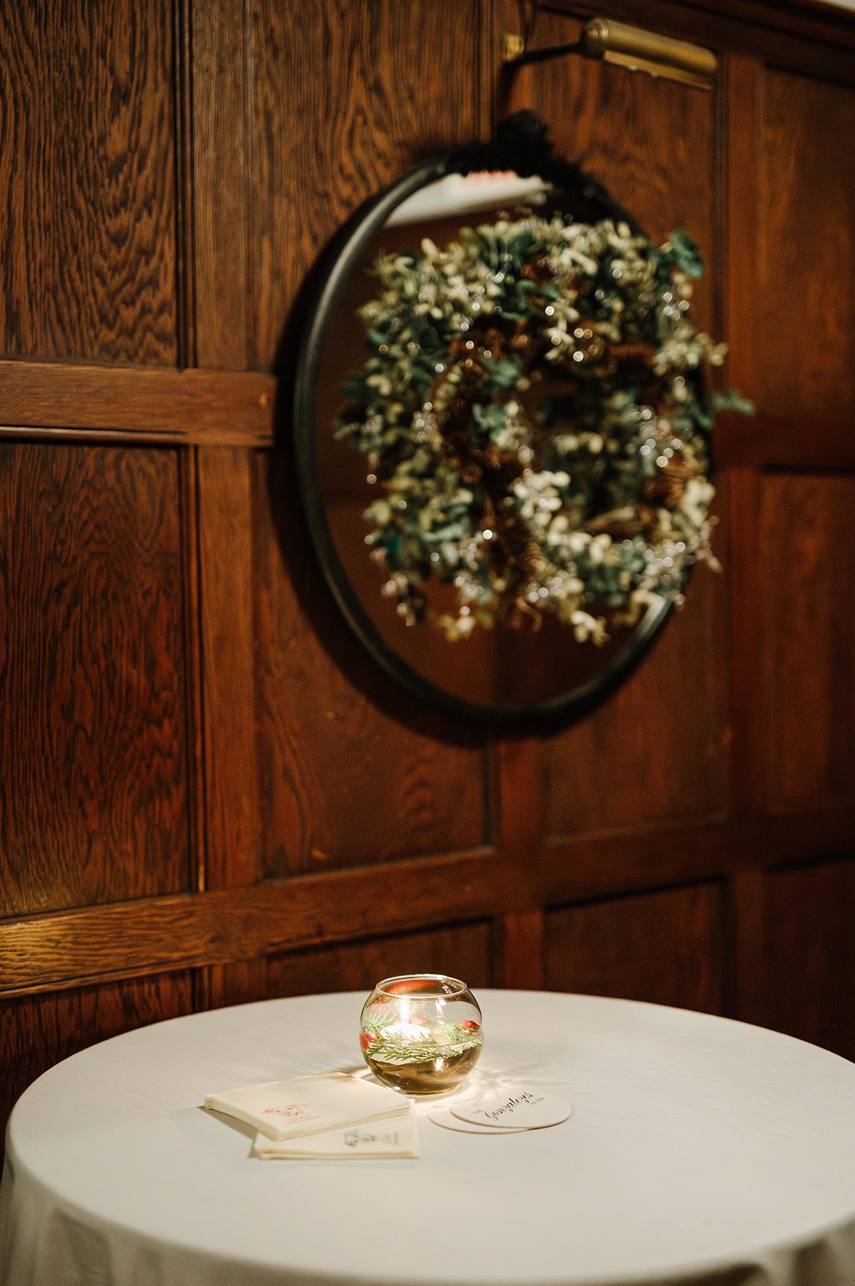 Oval mirror reflecting a floral wreath above a table with a small candle.