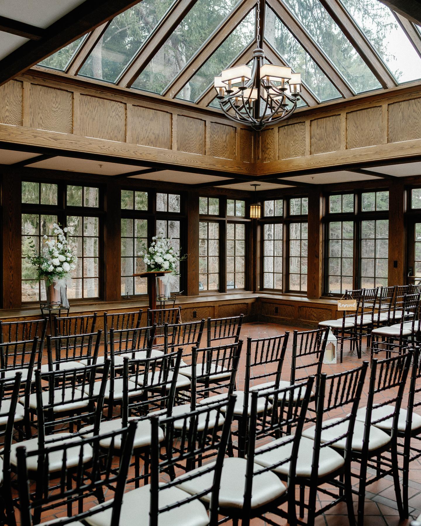 Sunlit glass-roofed dining room with long tables and black wooden chairs