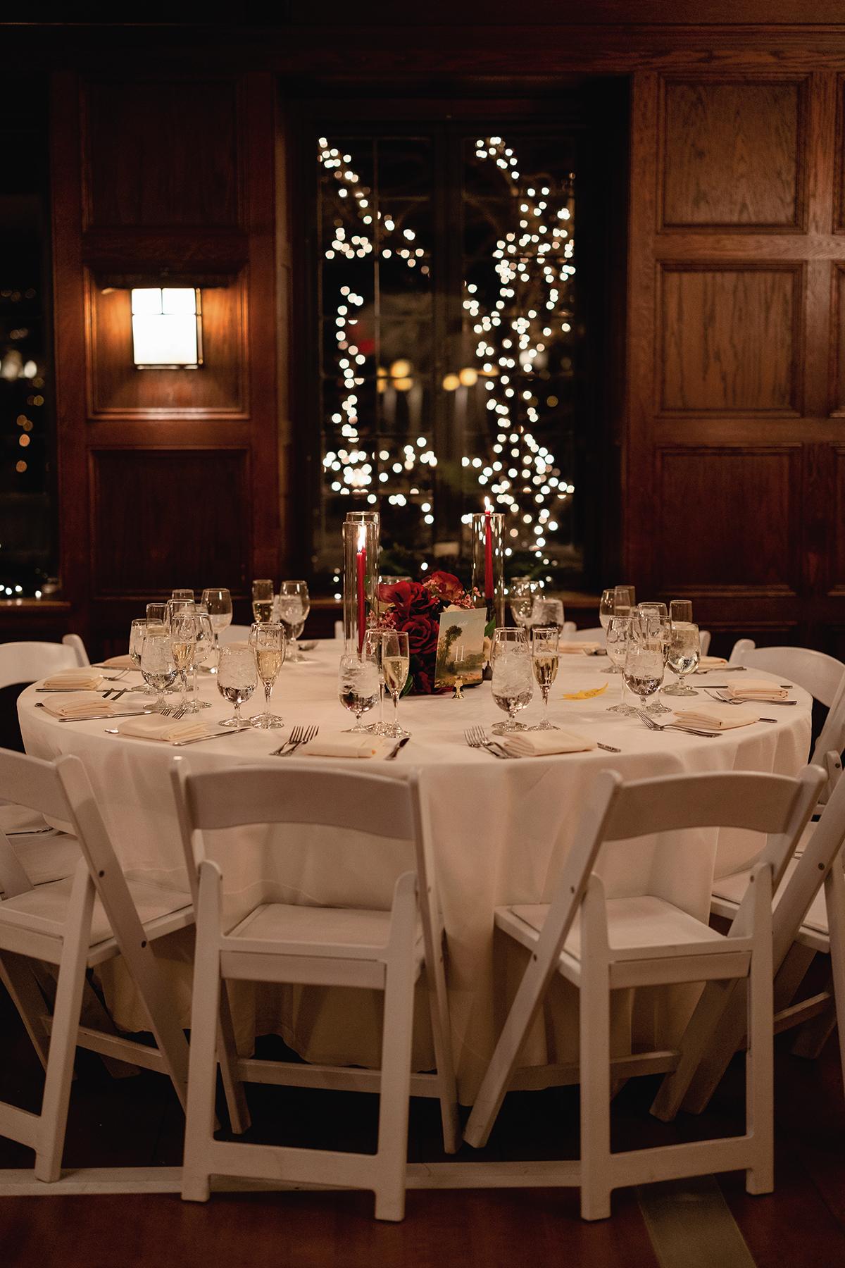 Elegant banquet table set for dinner beneath a lit Christmas tree in a wood-paneled room.
